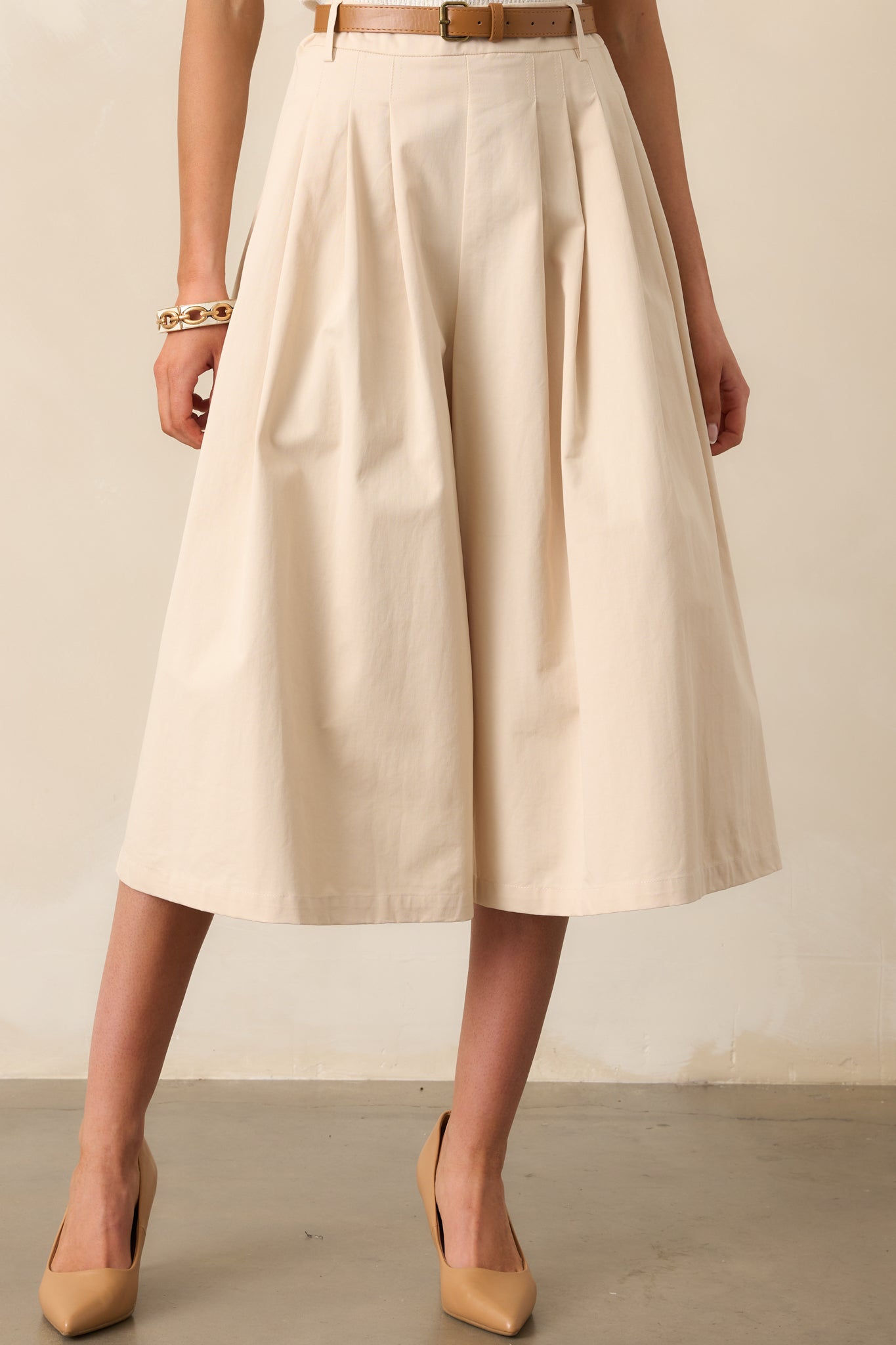 A closer look at the pleated wide-leg design and functional belt loops of these beige pants.