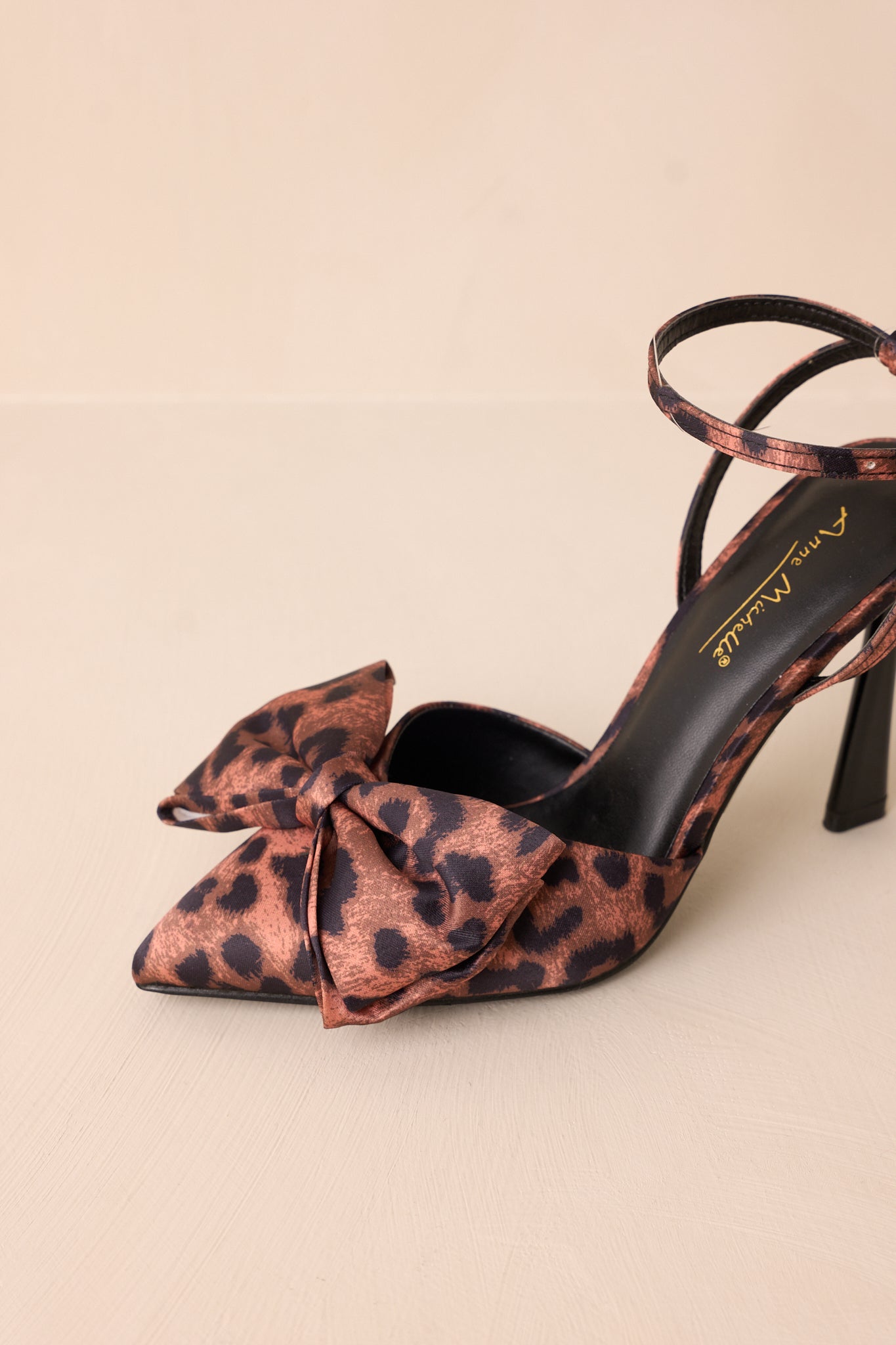 Close-up of the heels showing the bow detail, leopard print pattern, and gold buckle on the ankle strap.