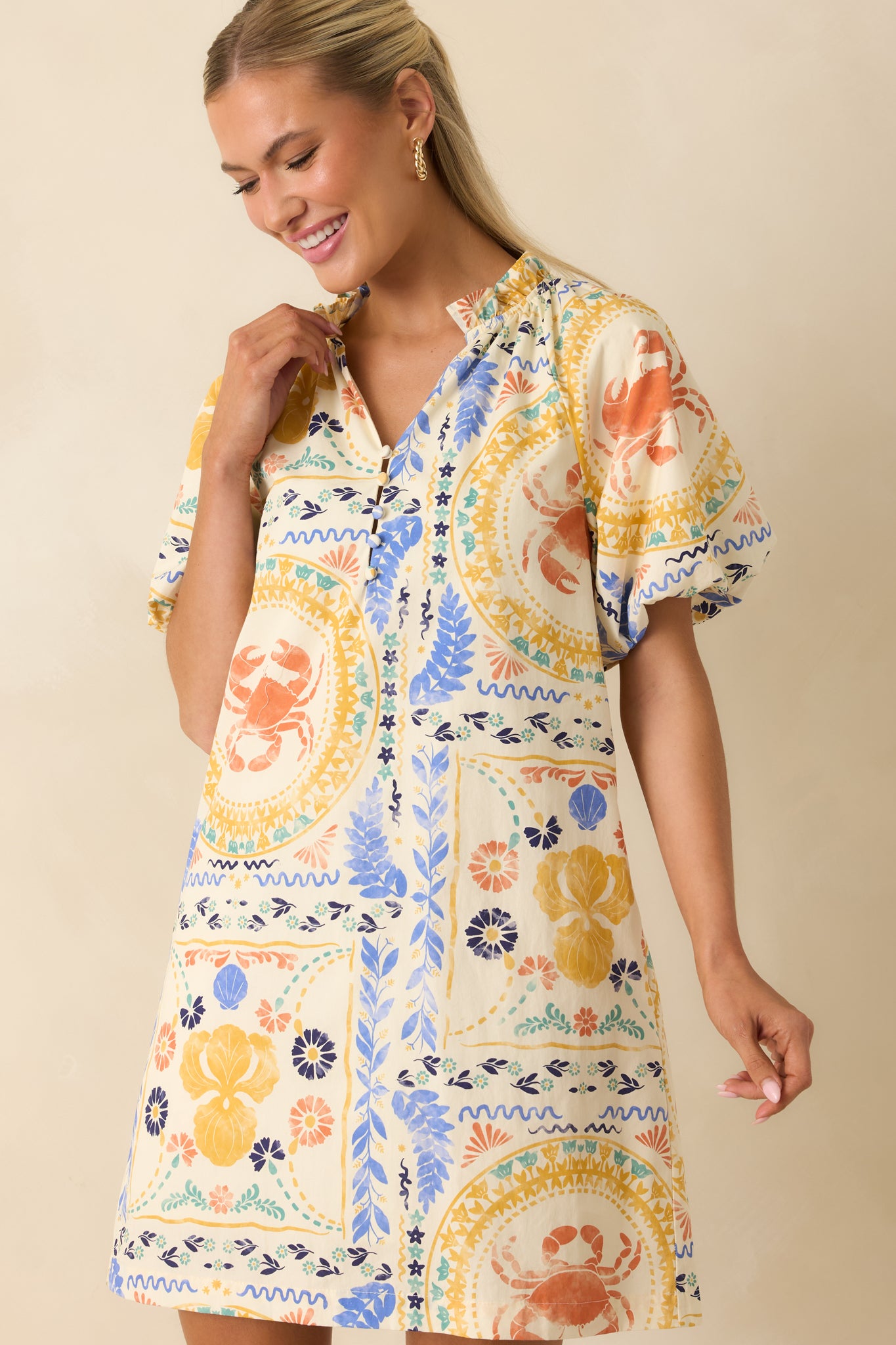 Close view of the mini dress highlighting the split neckline, stand collar, decorative buttons, and colorful coastal patchwork print.