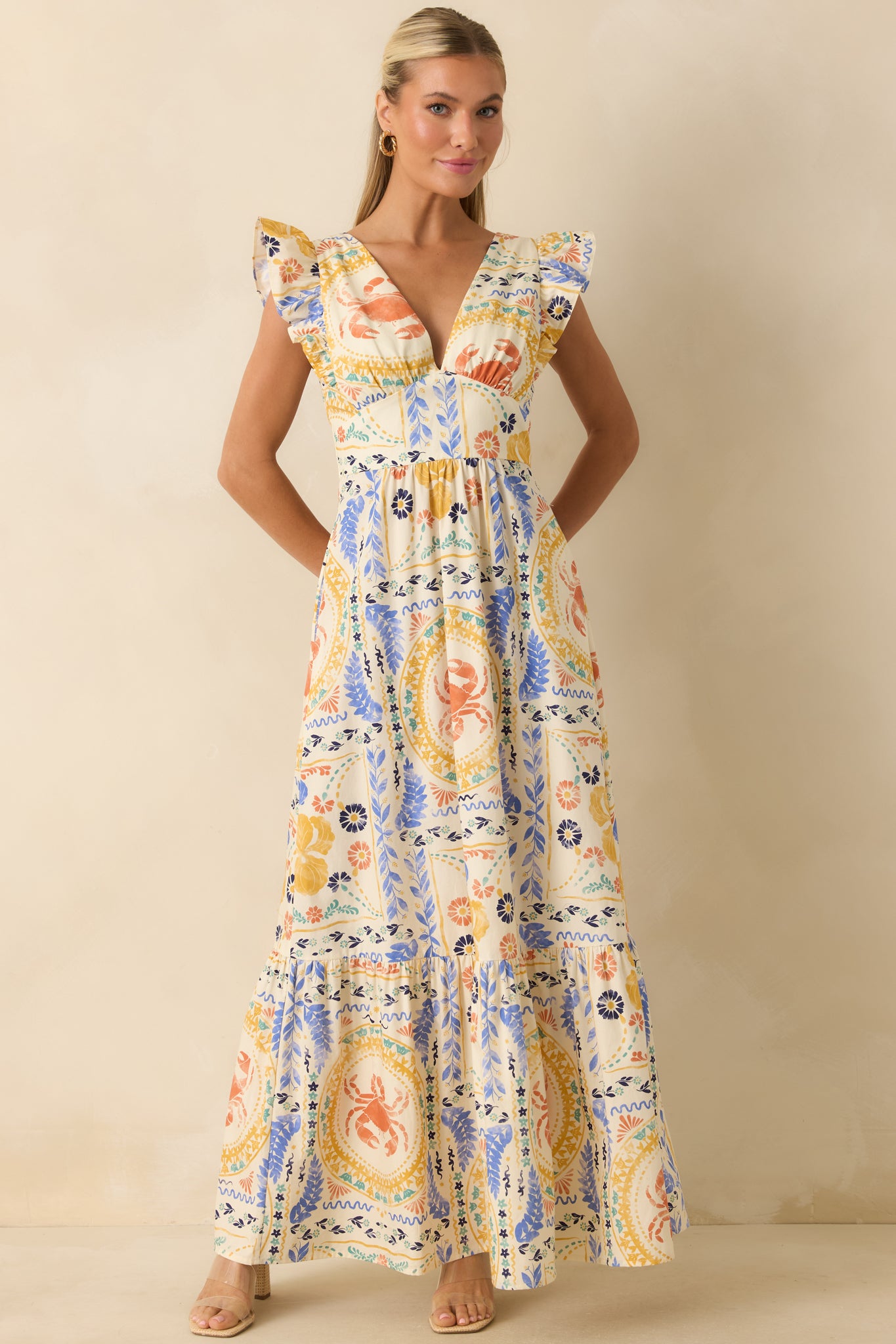 Patchwork maxi dress featuring coral, blue, yellow, and green coastal-inspired artwork, a defined waist, and a tiered full-length silhouette.