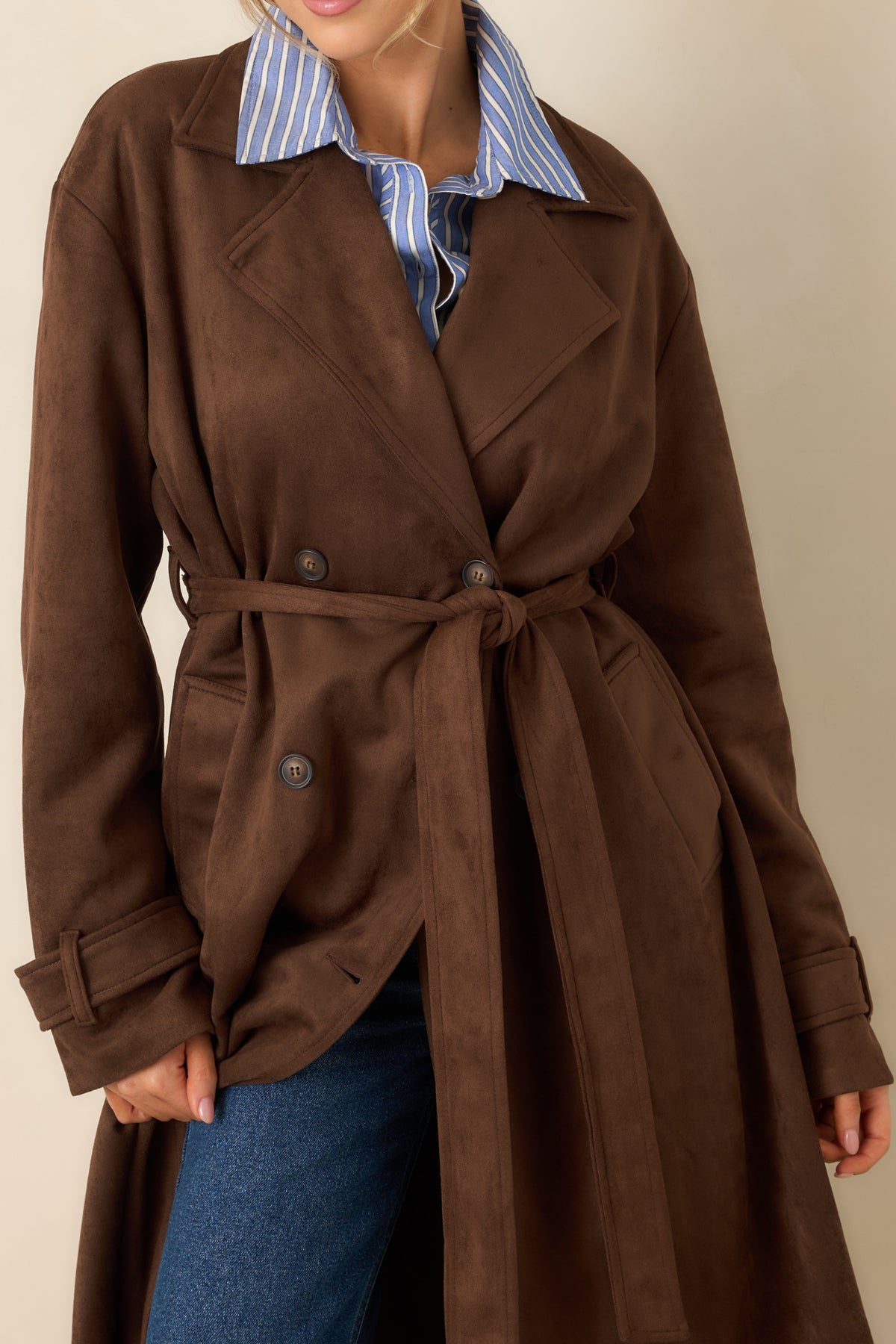 Close-up highlights the notched collar, double-breasted buttons, matching tie belt, and buttoned sleeve cuff tabs.