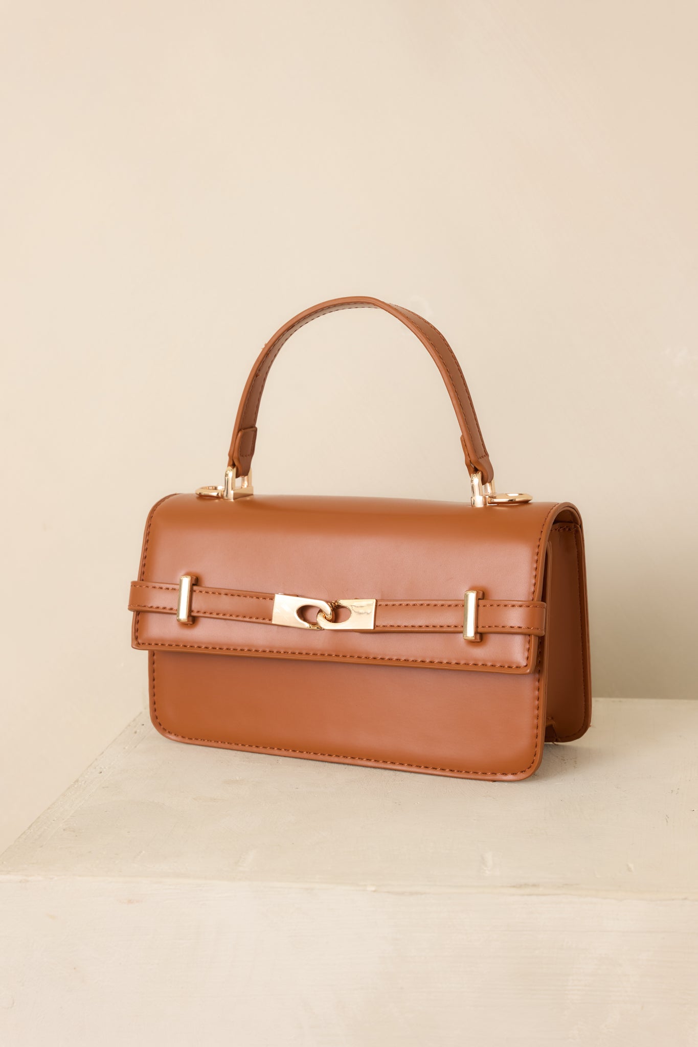 Cognac handbag featuring a refined rectangular shape, elegant top handle, gold-tone accents, front belt detail, and versatile shoulder strap.