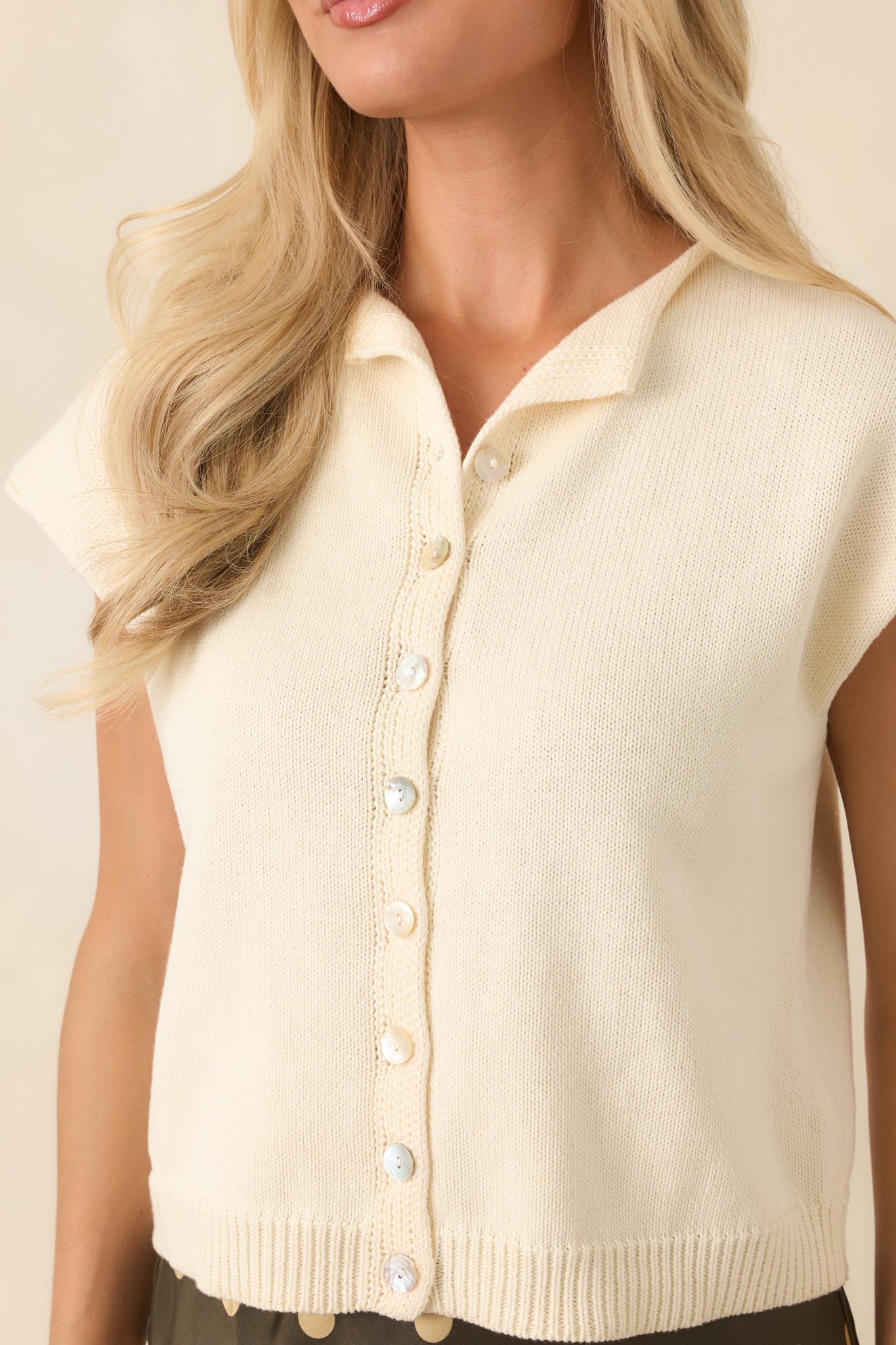 Close-up detail of the collar, pearlescent buttons, and ribbed knit texture on the top.