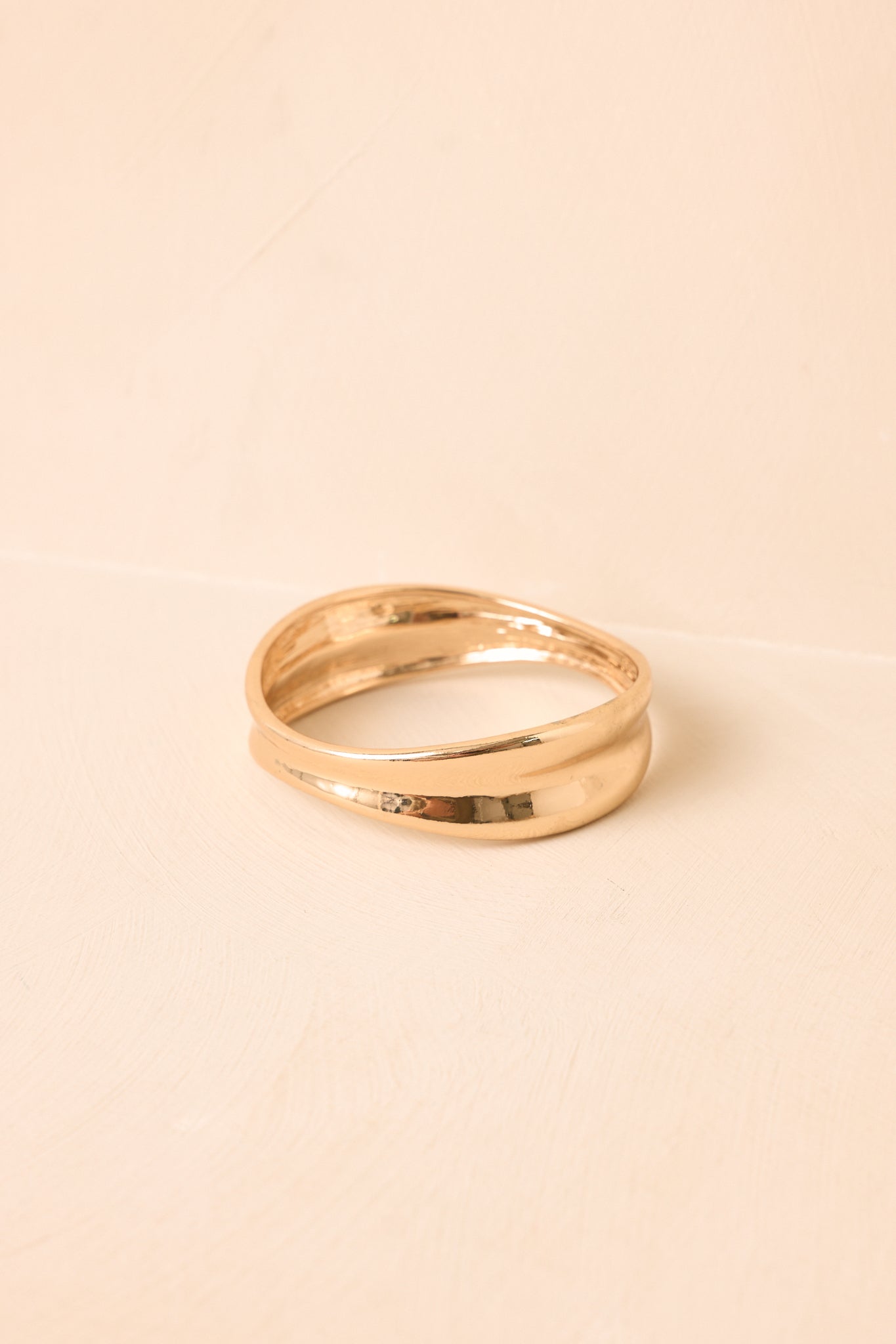 Concave bangle displayed against a beige background, highlighting its sculptural form and alternating widths.