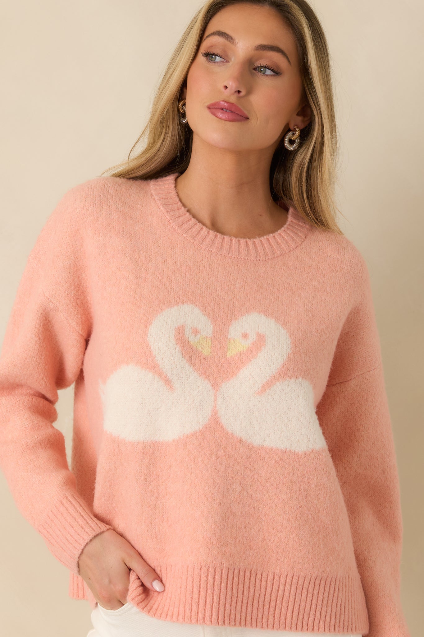 Coral knit sweater emphasizing the intricate intarsia swan heart motif and clean ribbed trim along the neckline.