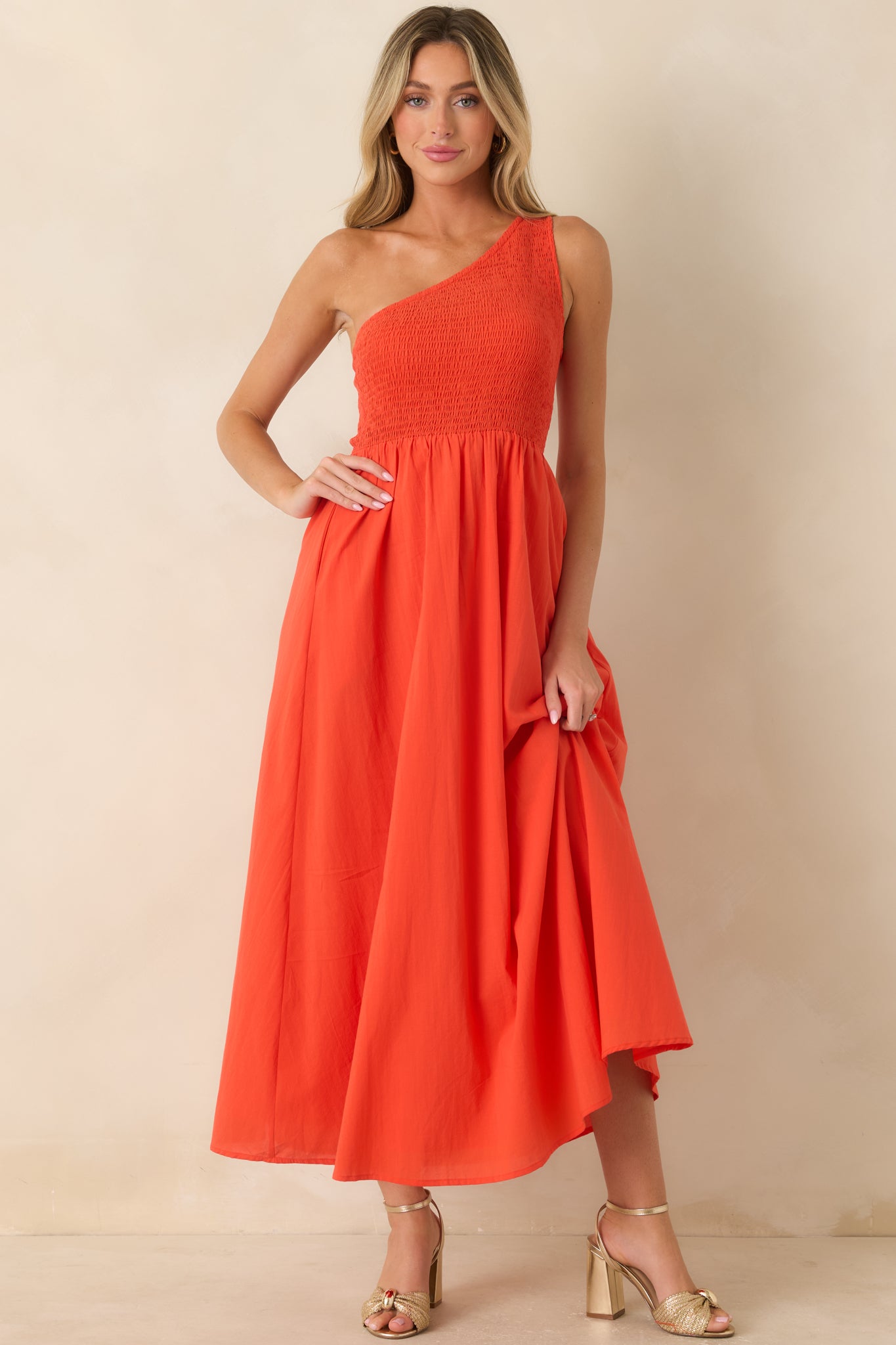Coral-orange cotton maxi dress featuring a softly gathered A-line skirt, textured smocked bodice, asymmetrical one-shoulder neckline, and hidden side pockets.