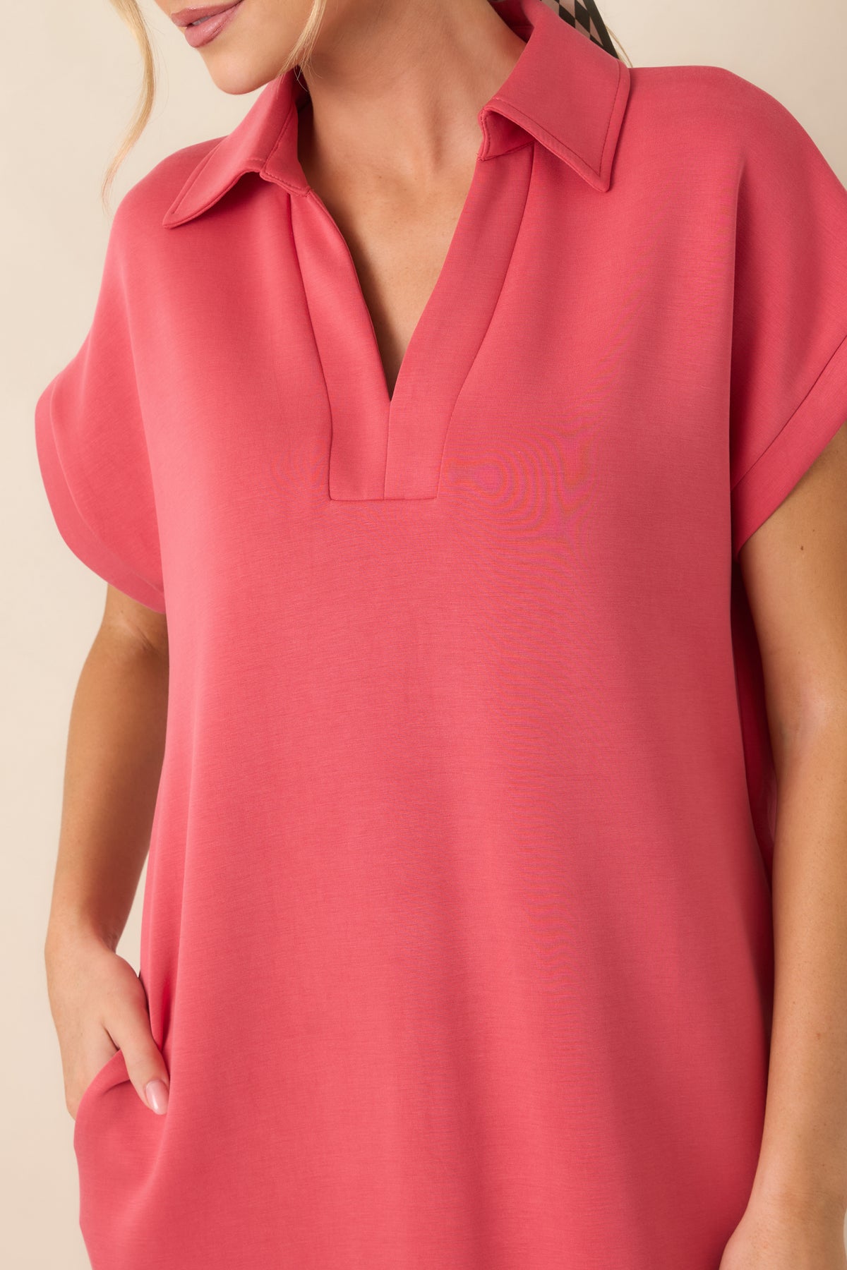 Close-up of the coral pink dress highlighting the collared notch V-neckline, soft fabric texture, and short sleeve construction.