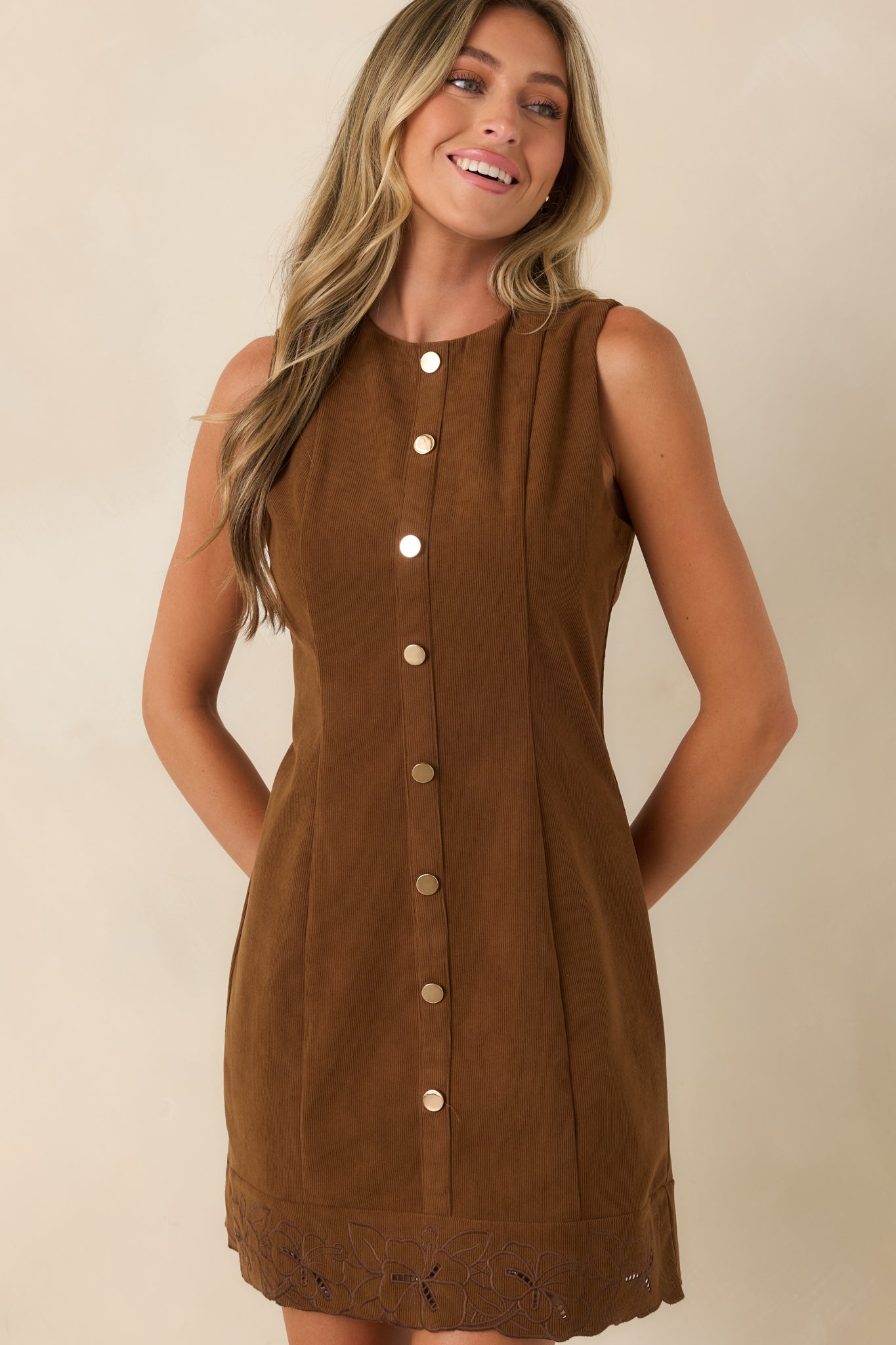 Close view of the corduroy mini dress featuring the round neckline, decorative button front, and embroidered scalloped hem.