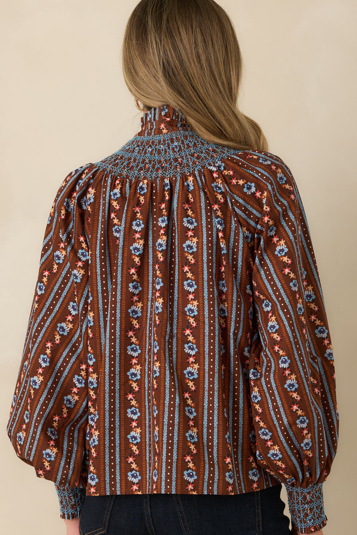 Rear view of the cotton blouse featuring contrasting blue smocking across the back yoke and gentle gathers below.