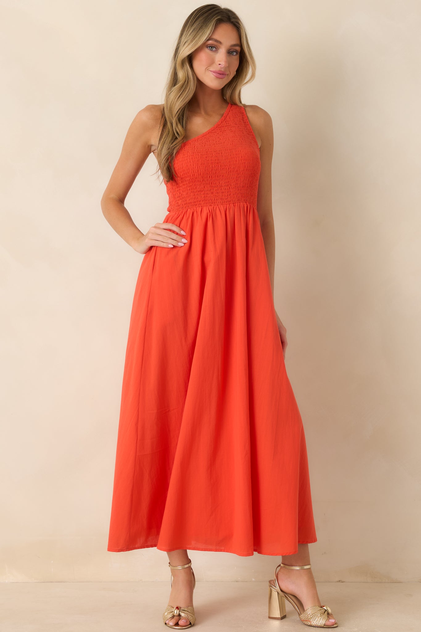 Cotton maxi dress in a vivid coral-orange hue featuring a flattering smocked bodice, elegant one-shoulder neckline, and a softly draped skirt.