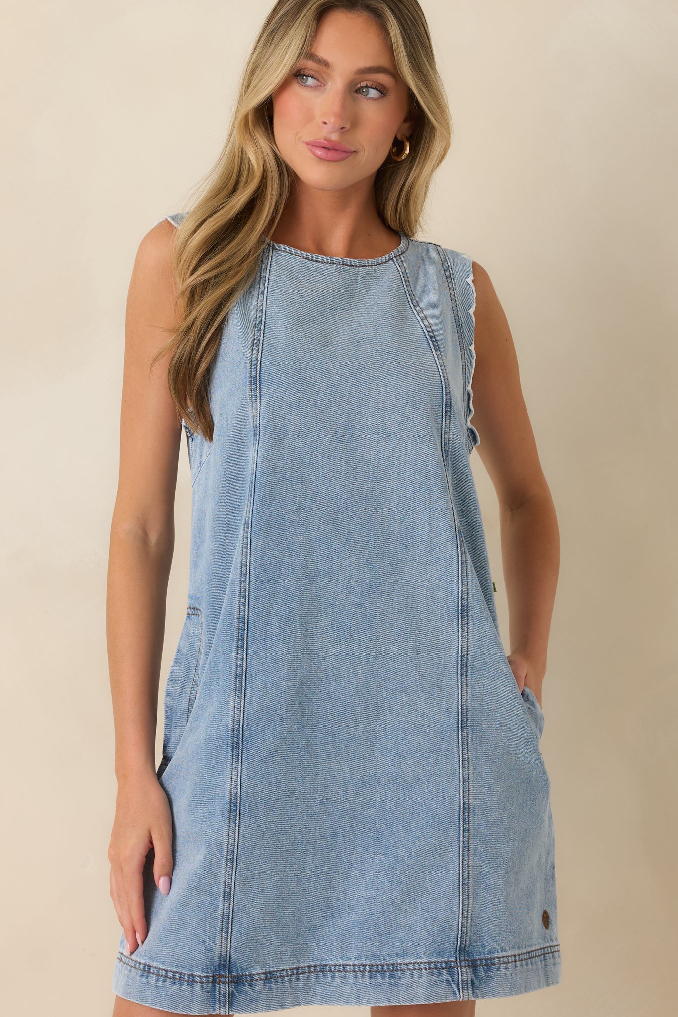 Close view of the cotton denim dress showcasing the sleeveless silhouette, light wash finish, and practical side pocket construction.