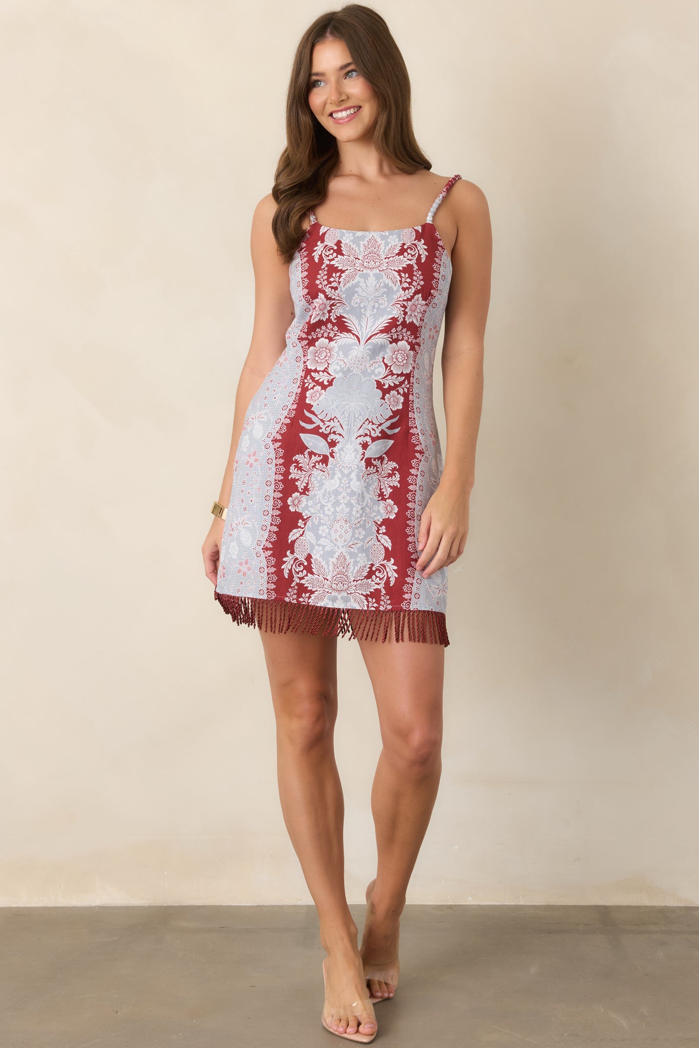 Cotton-linen mini dress showcasing a colorful border print, slender textured straps, and a gently fitted shape with fringe along the hem.
