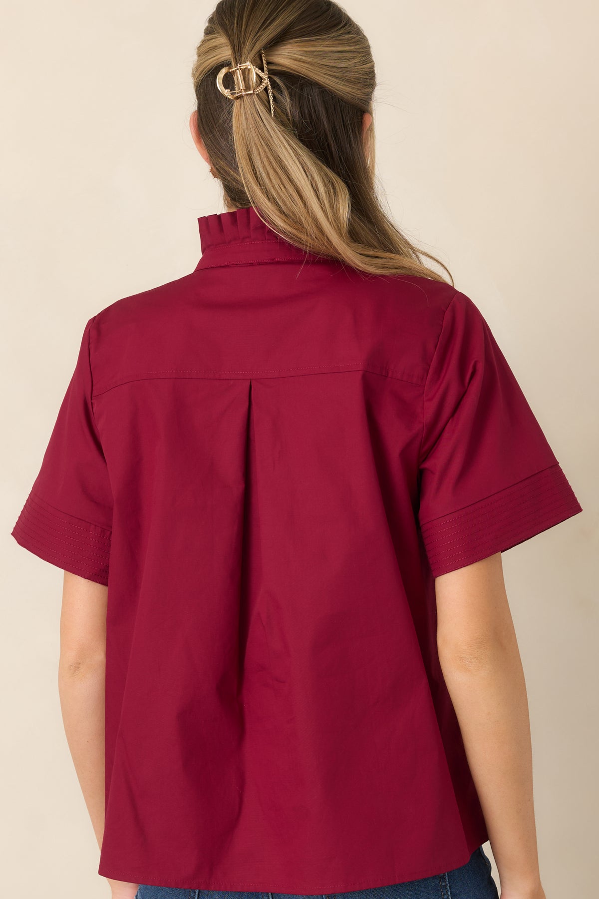 Rear view of the cotton top showcasing the center back pleat, relaxed drape, short sleeves, and polished silhouette.
