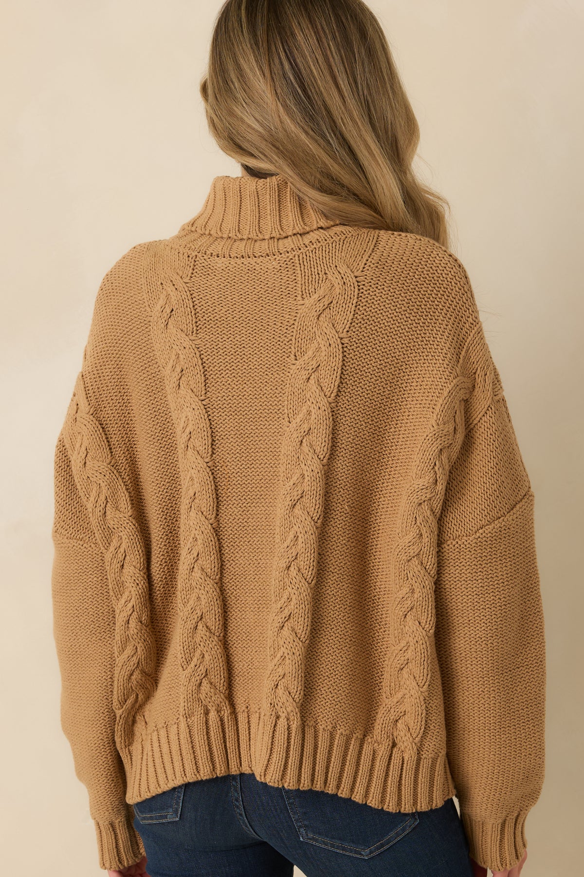 Rear view of the cozy sweater showcasing chunky cable detailing across the back, dropped shoulders, and ribbed hem.