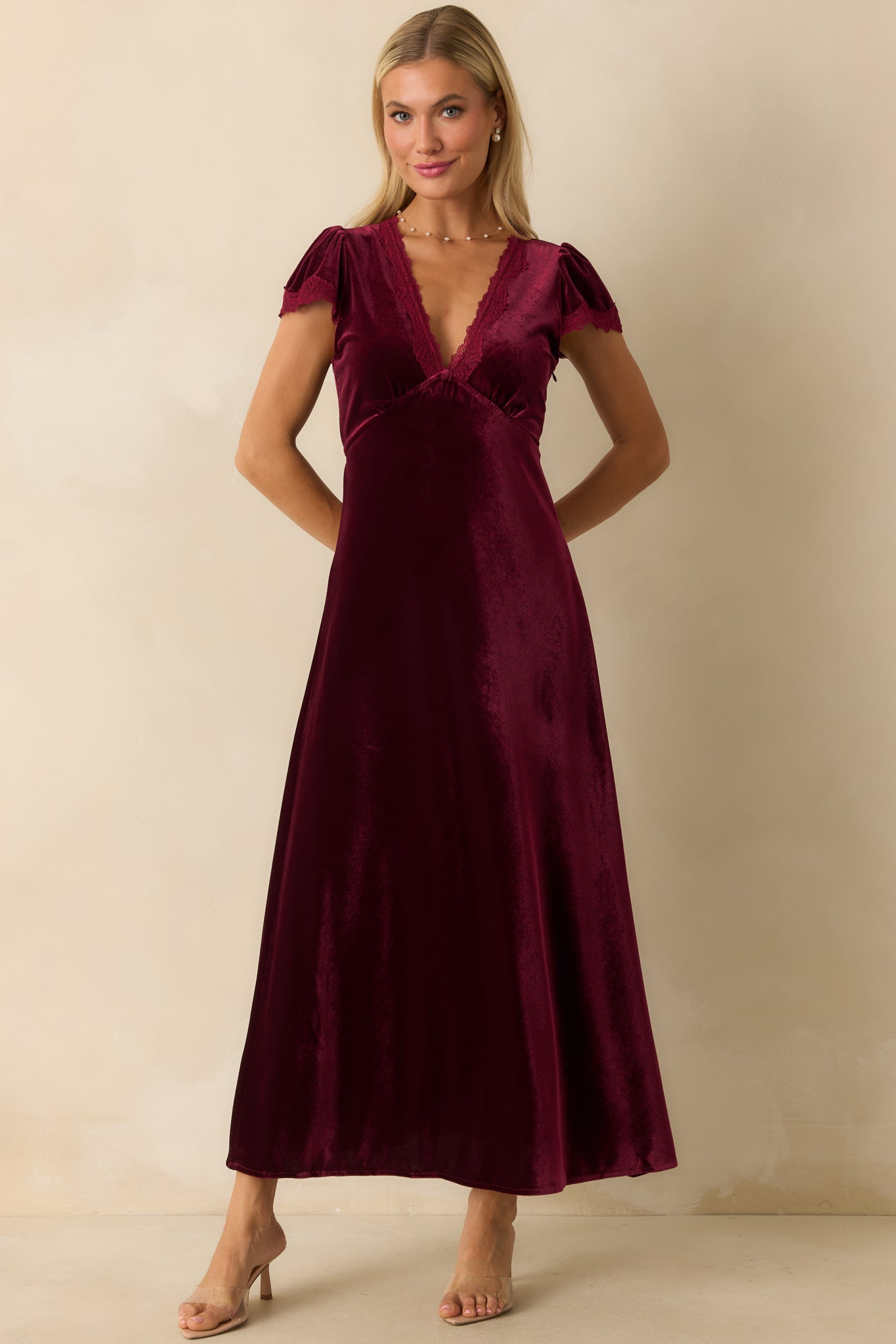 A-line cranberry red velvet dress with empire waist, flowing skirt, and lace-trimmed V-neckline.