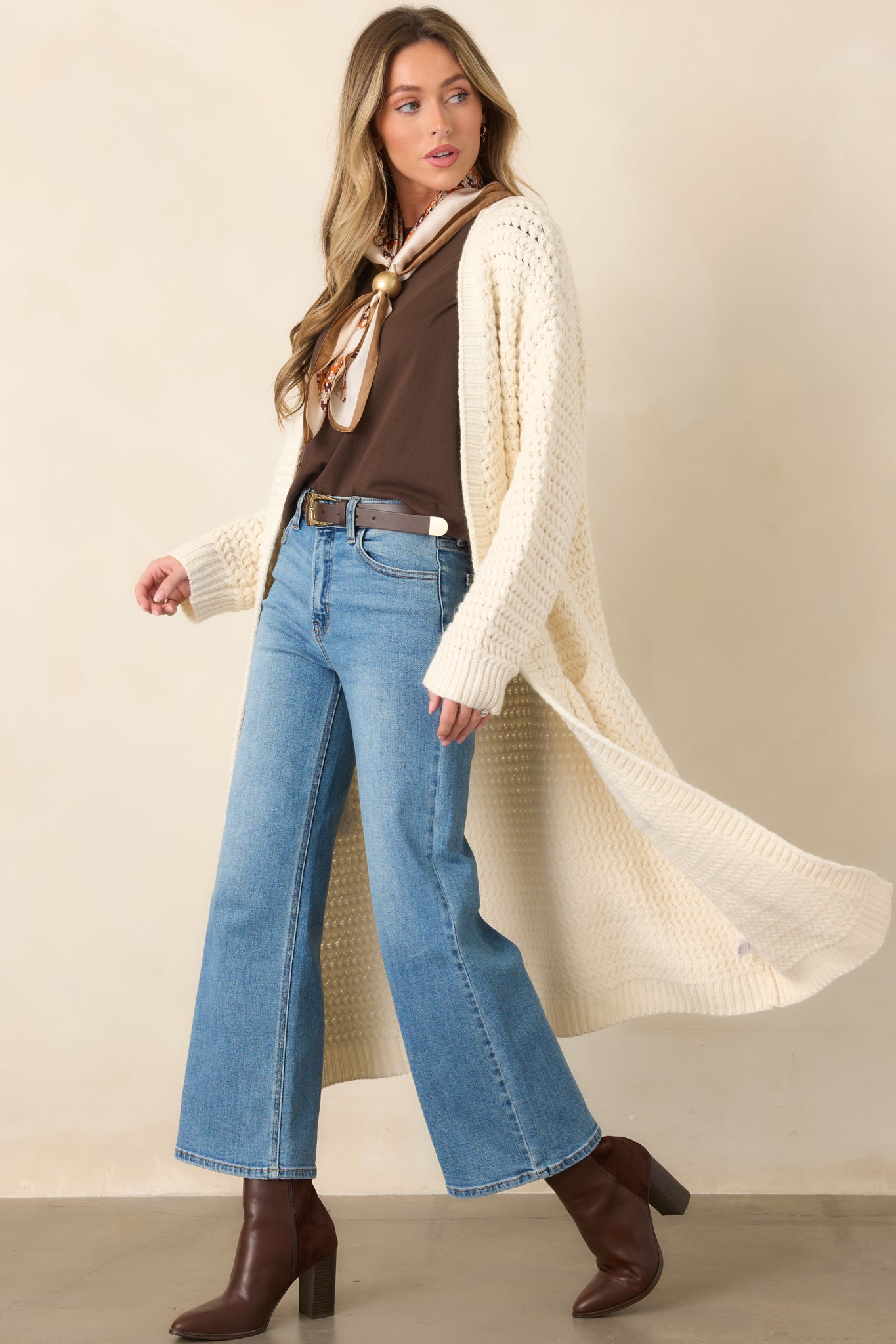 Cream knit duster cardigan with an open front, long sleeves, ribbed cuffs, patch pockets, and a relaxed longline silhouette.