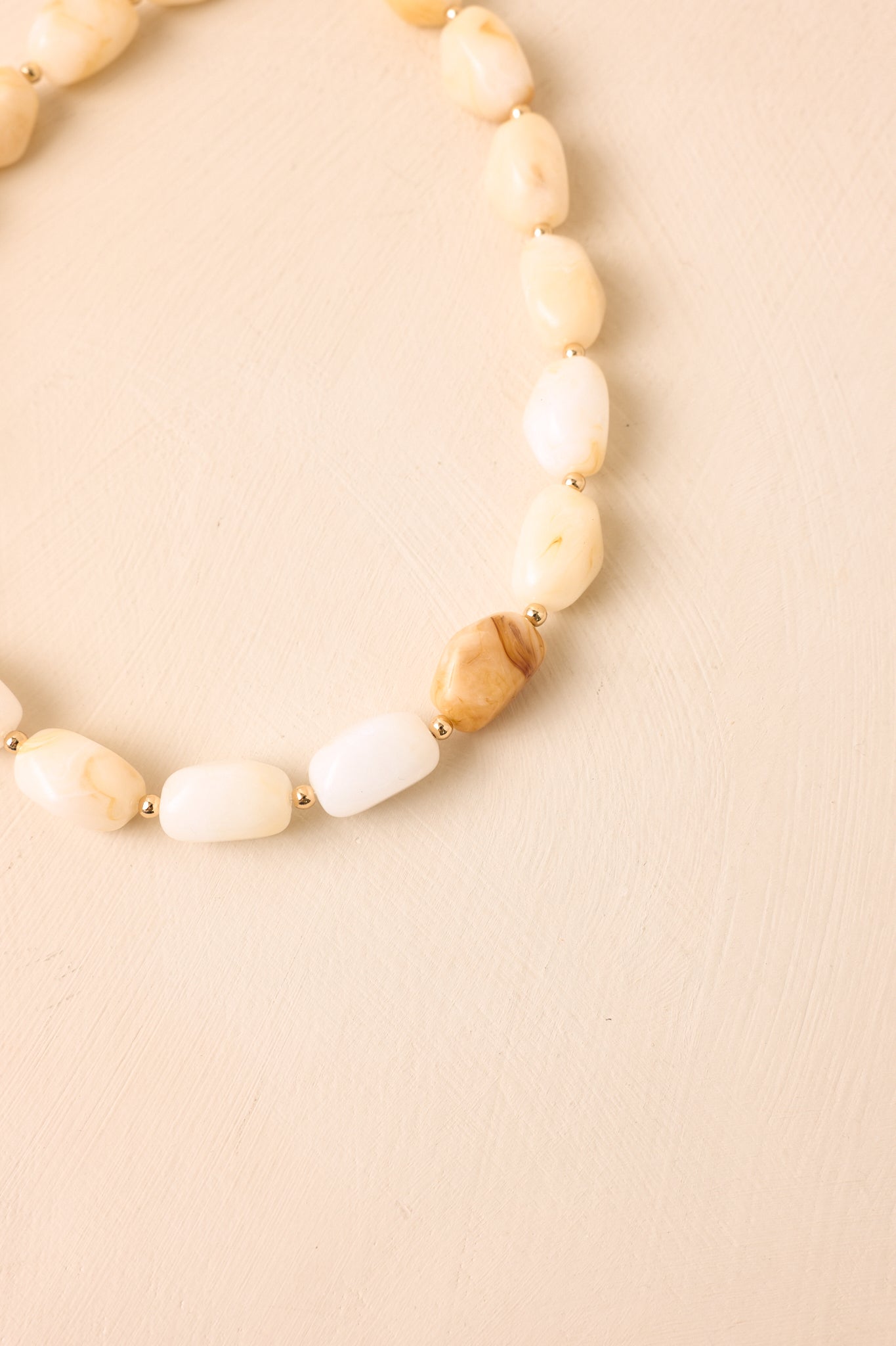 Cream resin necklace with gold-tone spacer beads presented against a neutral backdrop for an elegant finish.