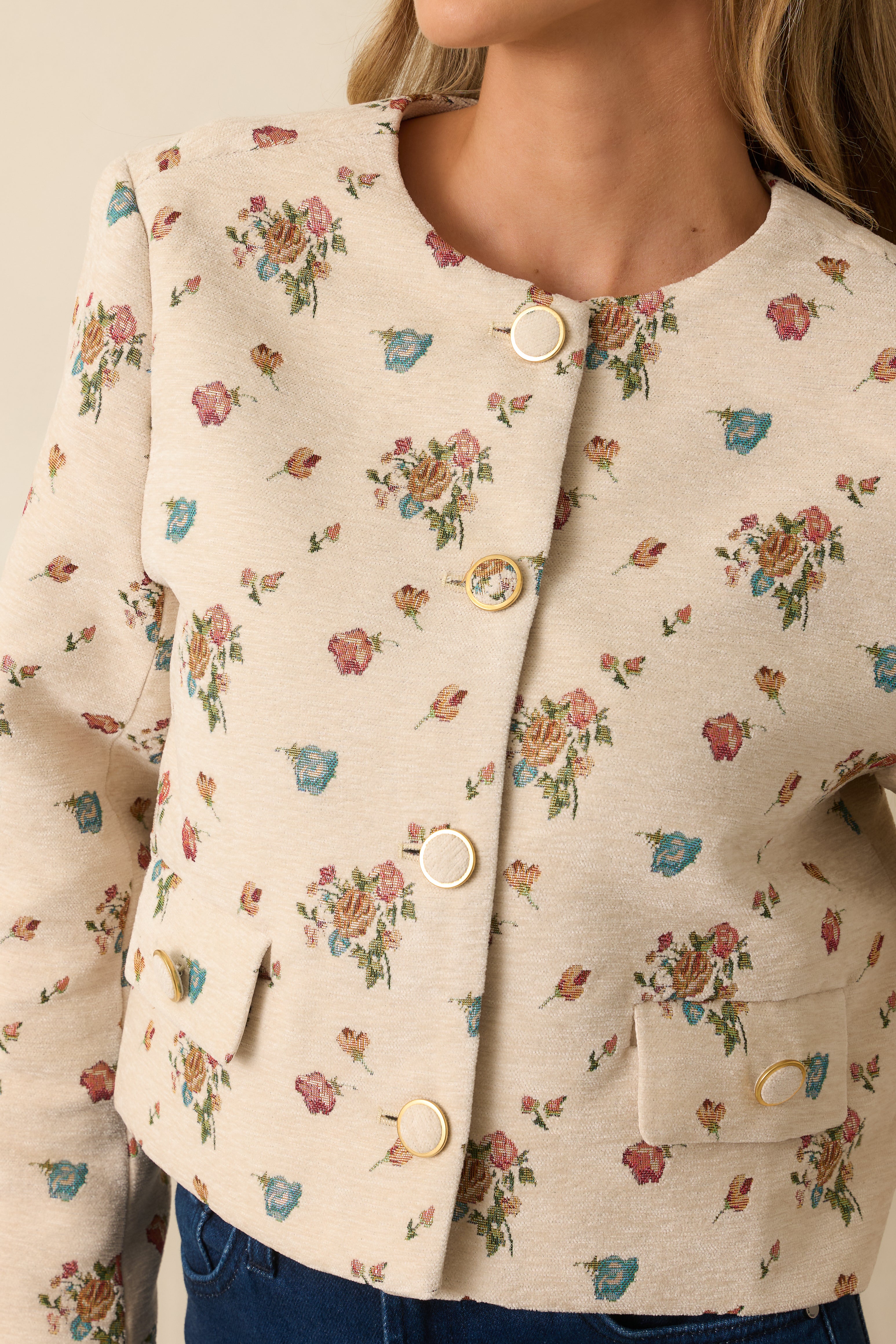 Close-up of the gold button closure and rich floral tapestry fabric on the cream jacket.
