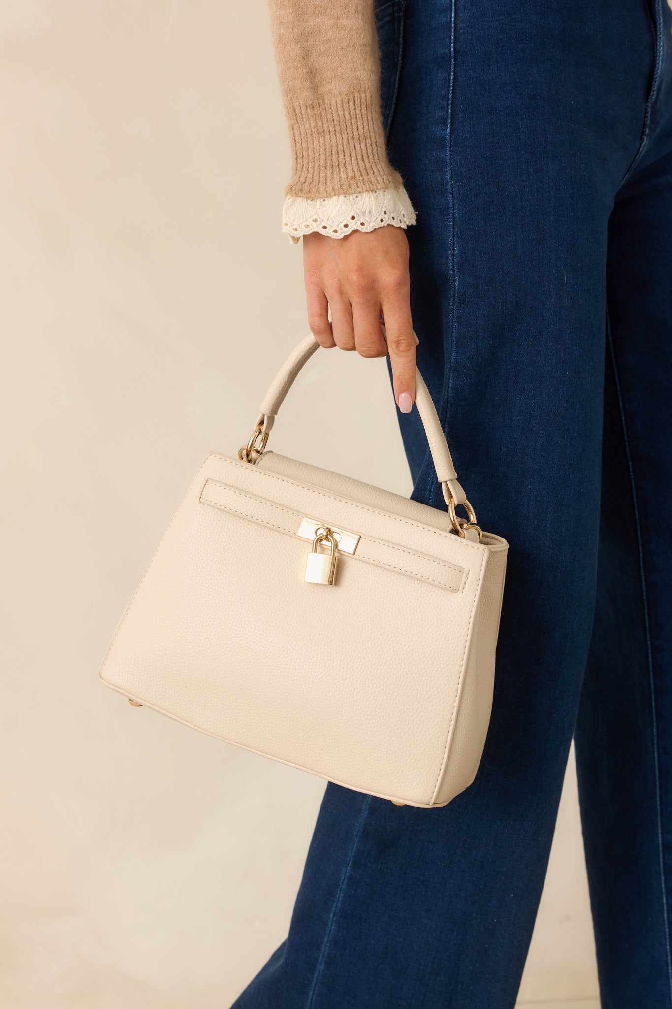 Cropped angle emphasizing the top handle, flap closure, and decorative lock on the nude handbag.