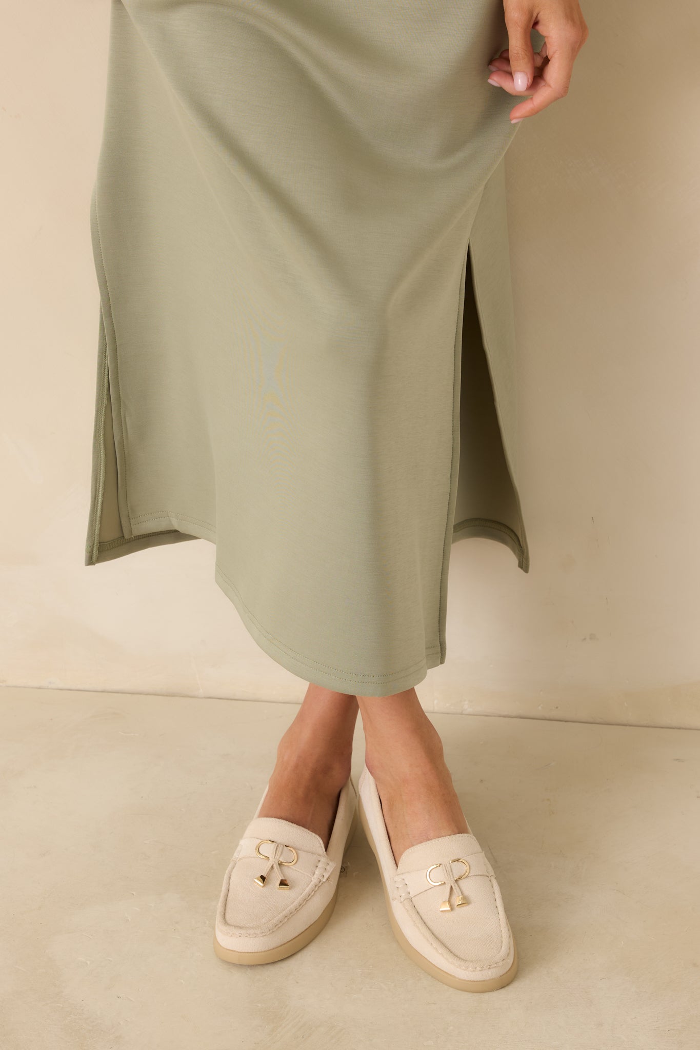 Cropped angle of ivory loafers showing the gold charm and smooth faux suede upper.