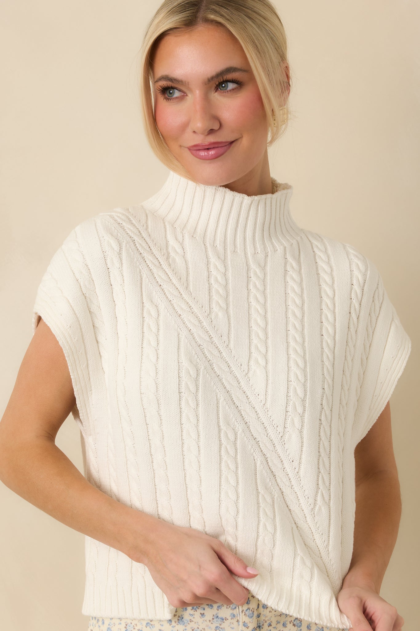 Front cropped angle of an ivory sleeveless knit top focusing on the textured cables and clean ribbed neckline.