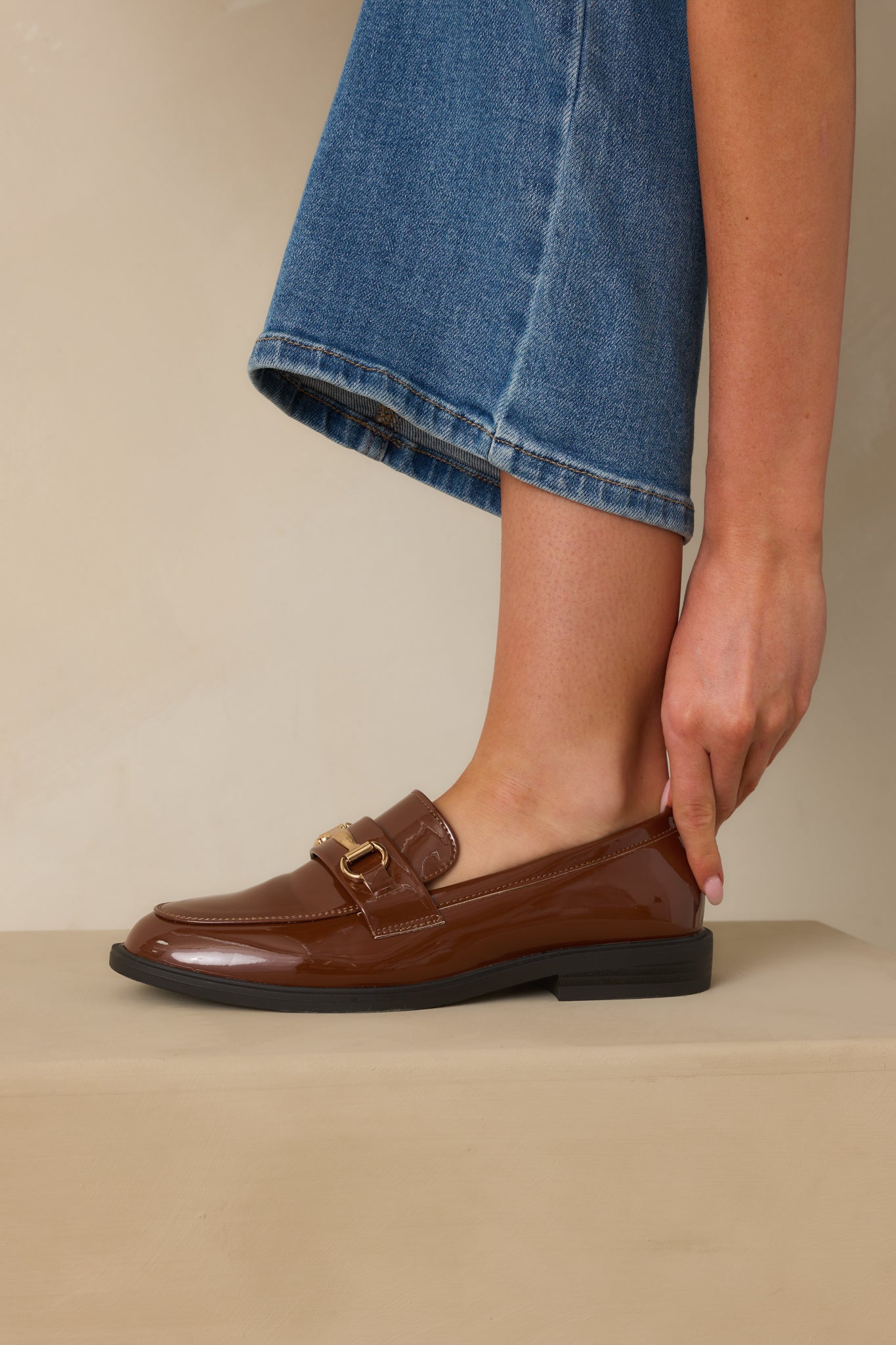 Cropped view of brown patent loafers highlighting the almond toe and sleek silhouette.
