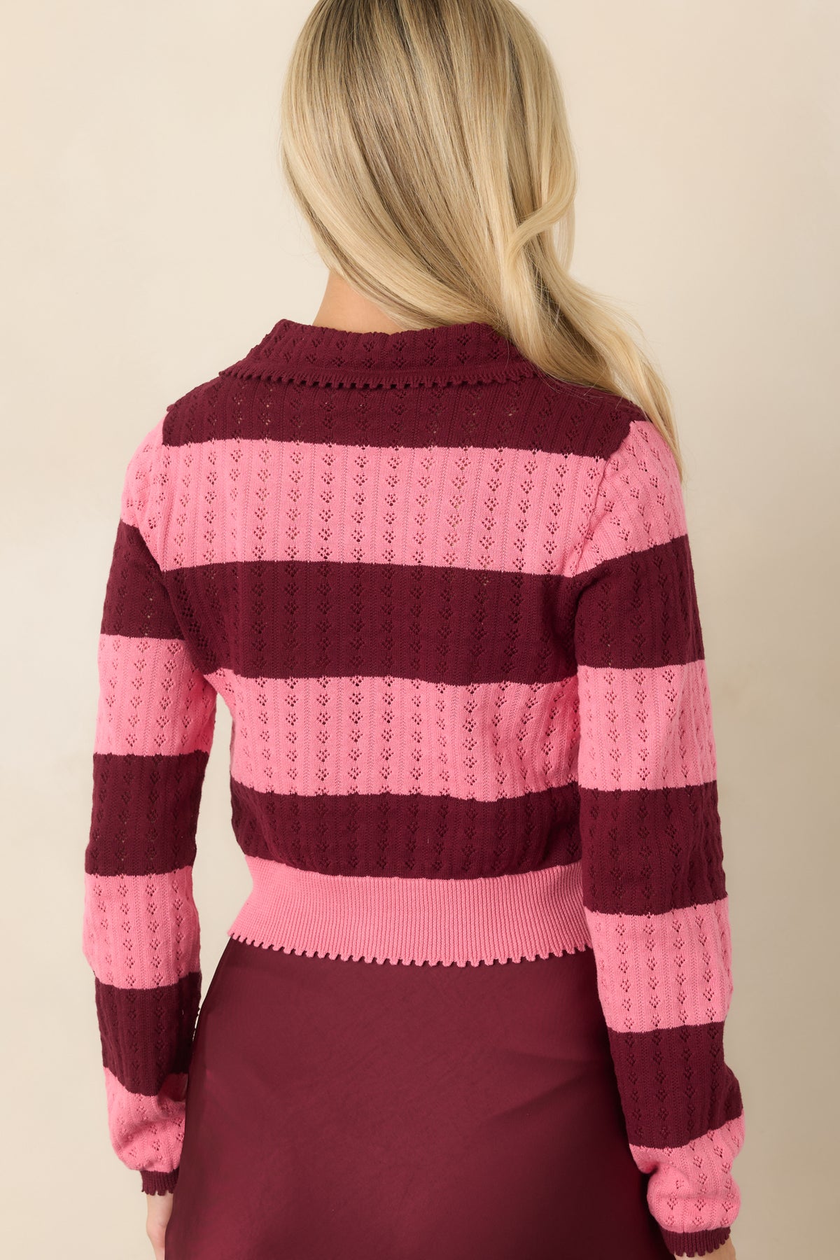 Rear of the cropped cotton cardigan featuring alternating wine and bright pink knit bands and long sleeves.