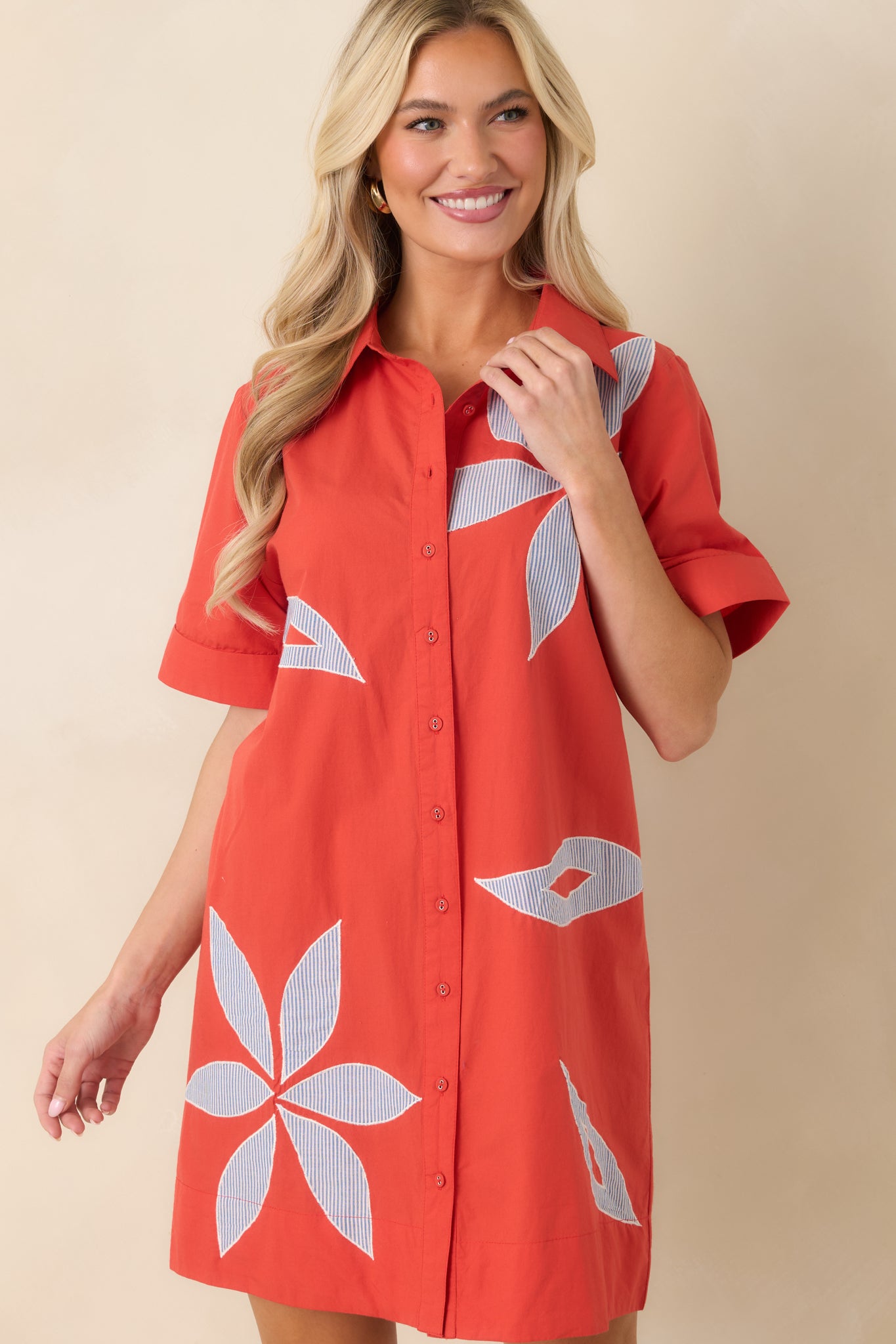 Cropped detail of blue and white striped dress highlighting bold floral appliqué and relaxed structure.