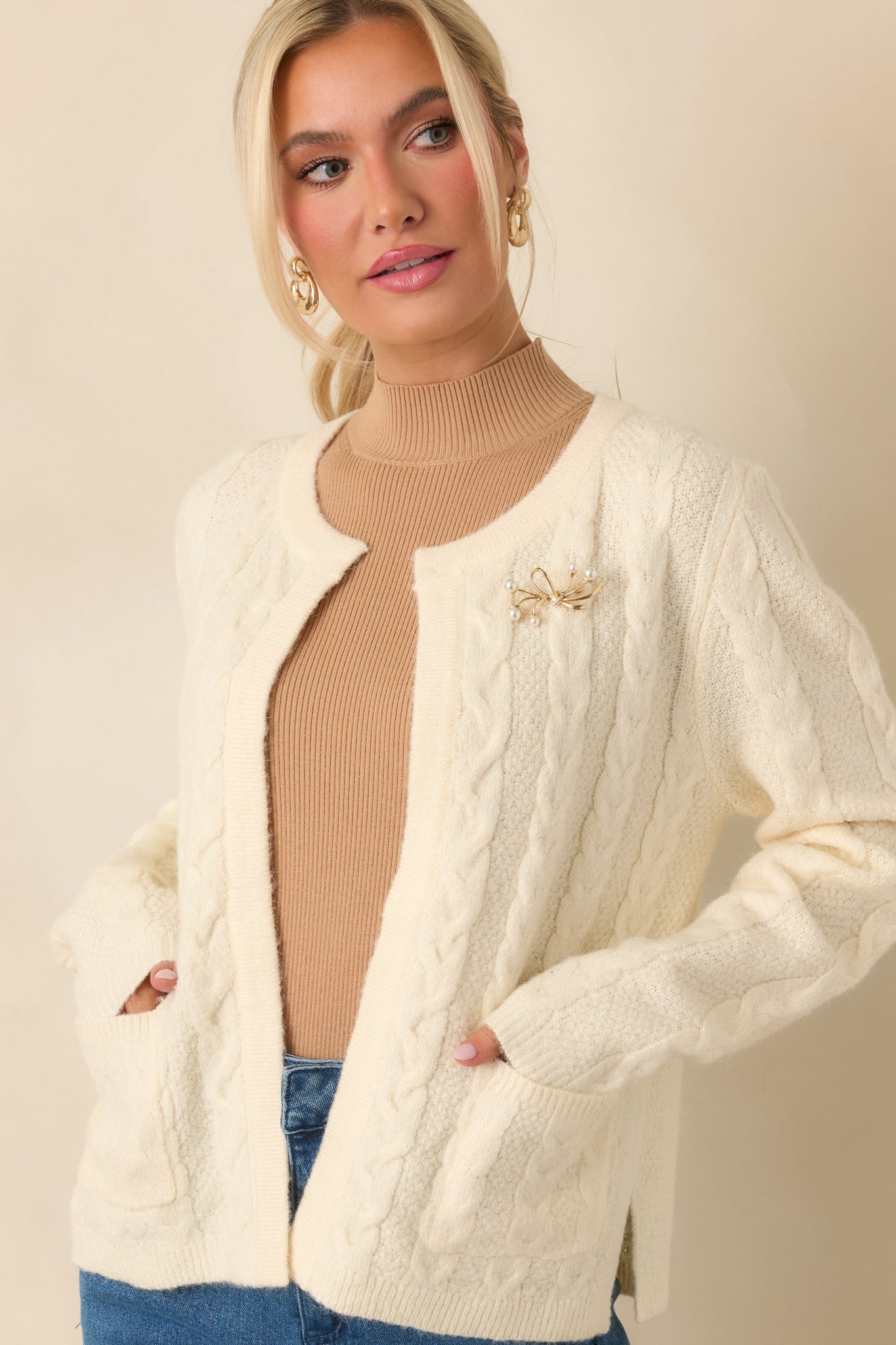 Cropped detail highlighting ribbed cuff and sleeve stitching on the soft ivory knit cardigan.