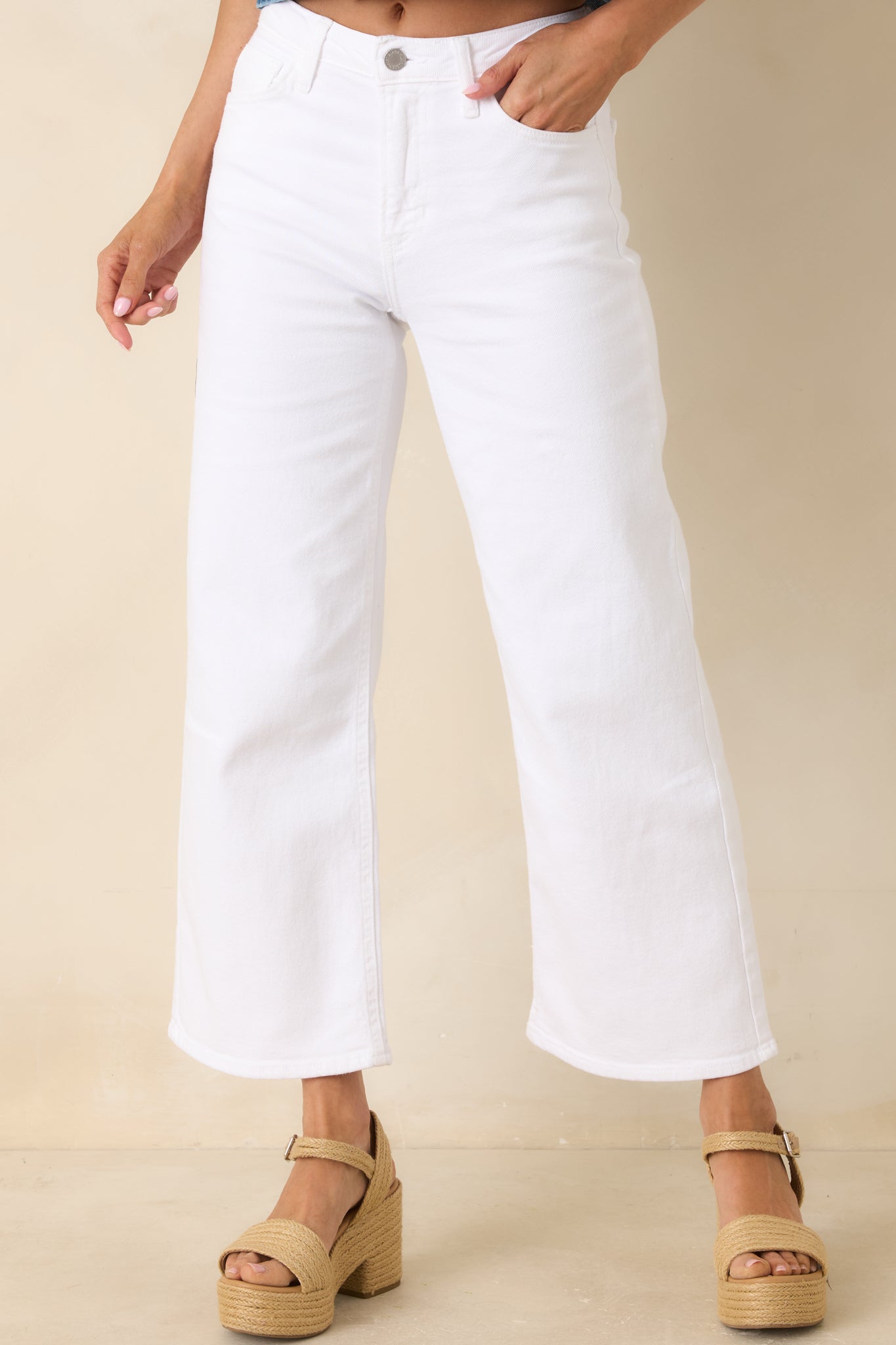 Close cropped detail of the front of white jeans showing the zip fly, button closure, and five-pocket styling