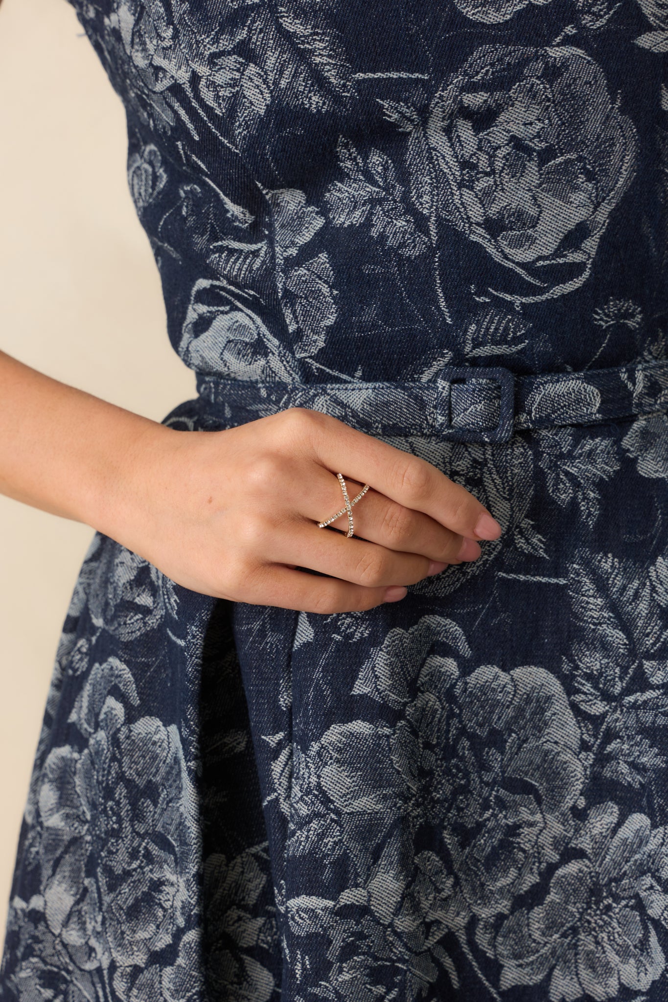 A cropped front view of the gold ring featuring a slim open band and intersecting rows of clear round-cut rhinestones.