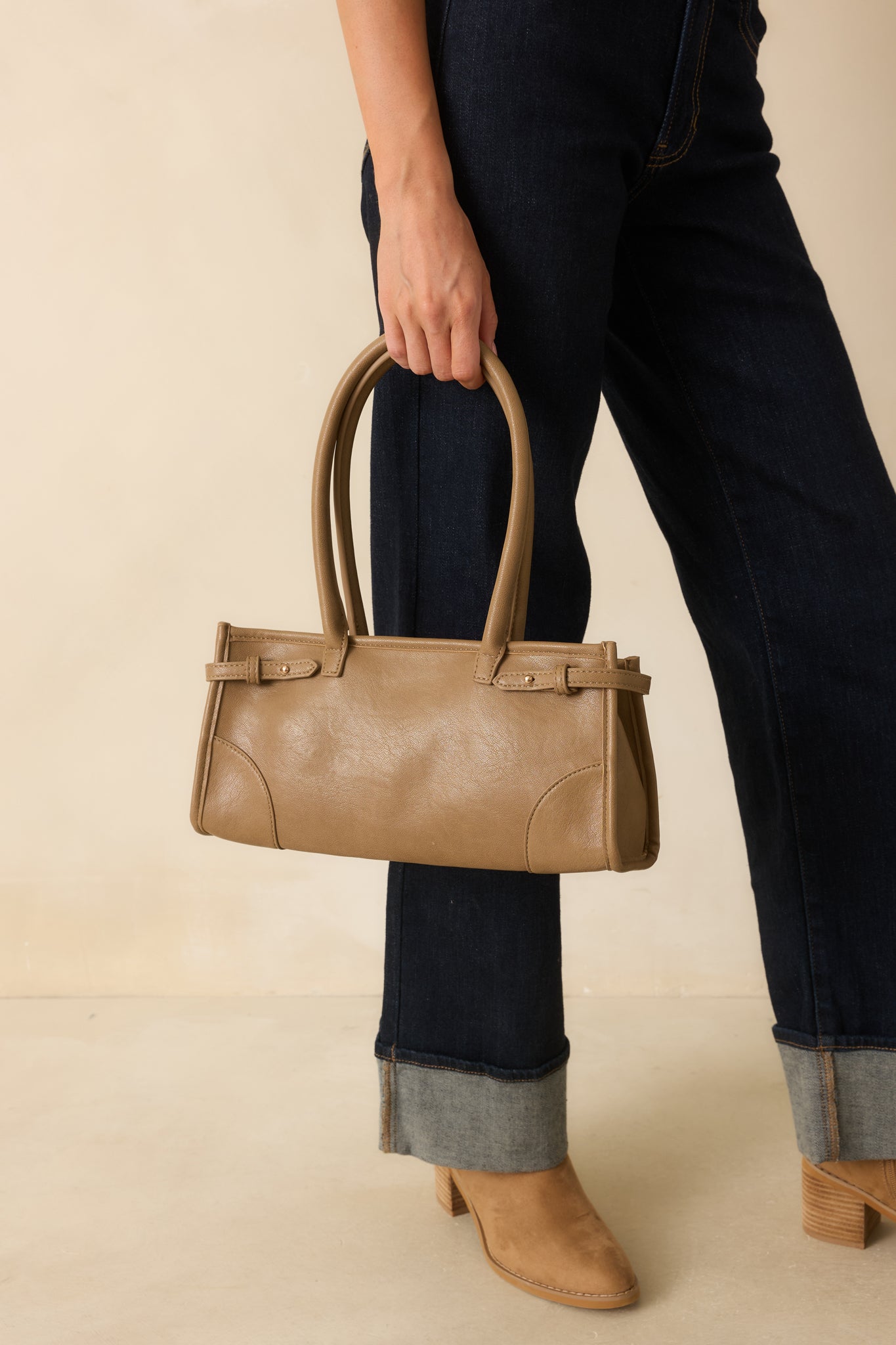 A cropped front view focusing on the top zip closure, belted side details, and handle attachment.