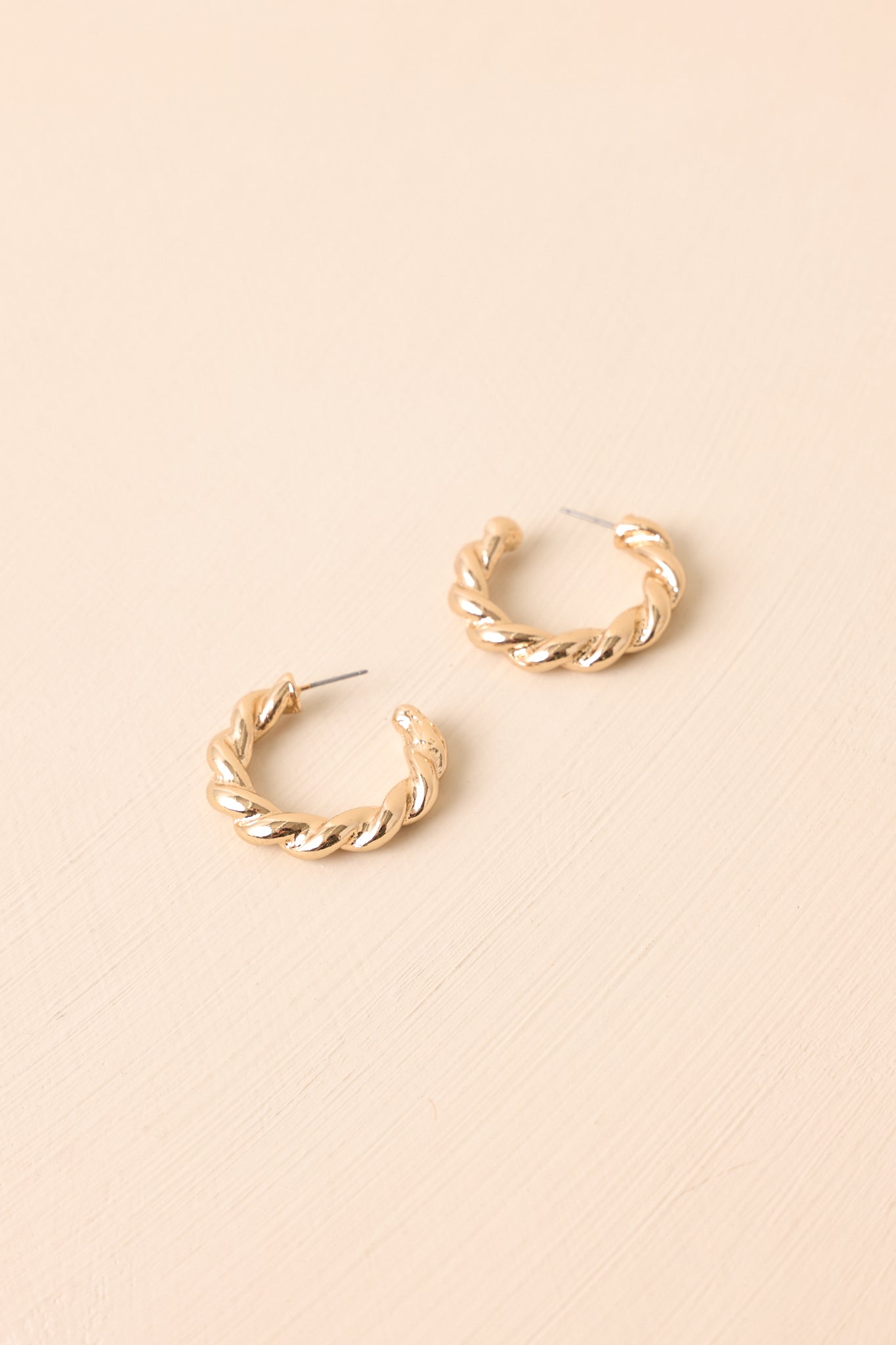 Cropped view of the gold twisted hoop earrings with open c-shaped design and post backing.