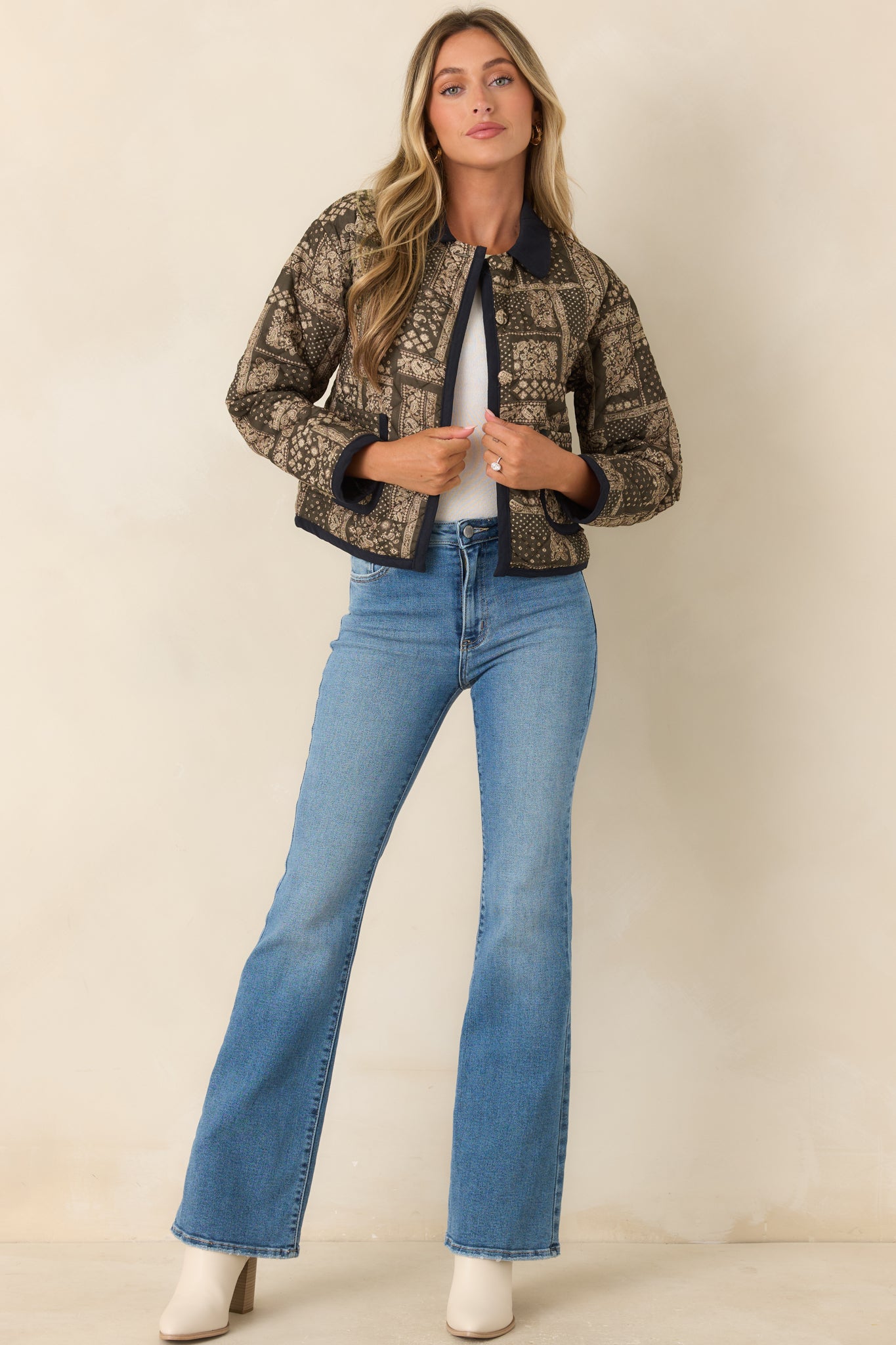 Cropped paisley jacket featuring a green and ivory patchwork print, contrasting pointed collar, dark trim, and an open-front silhouette with a single button closure.