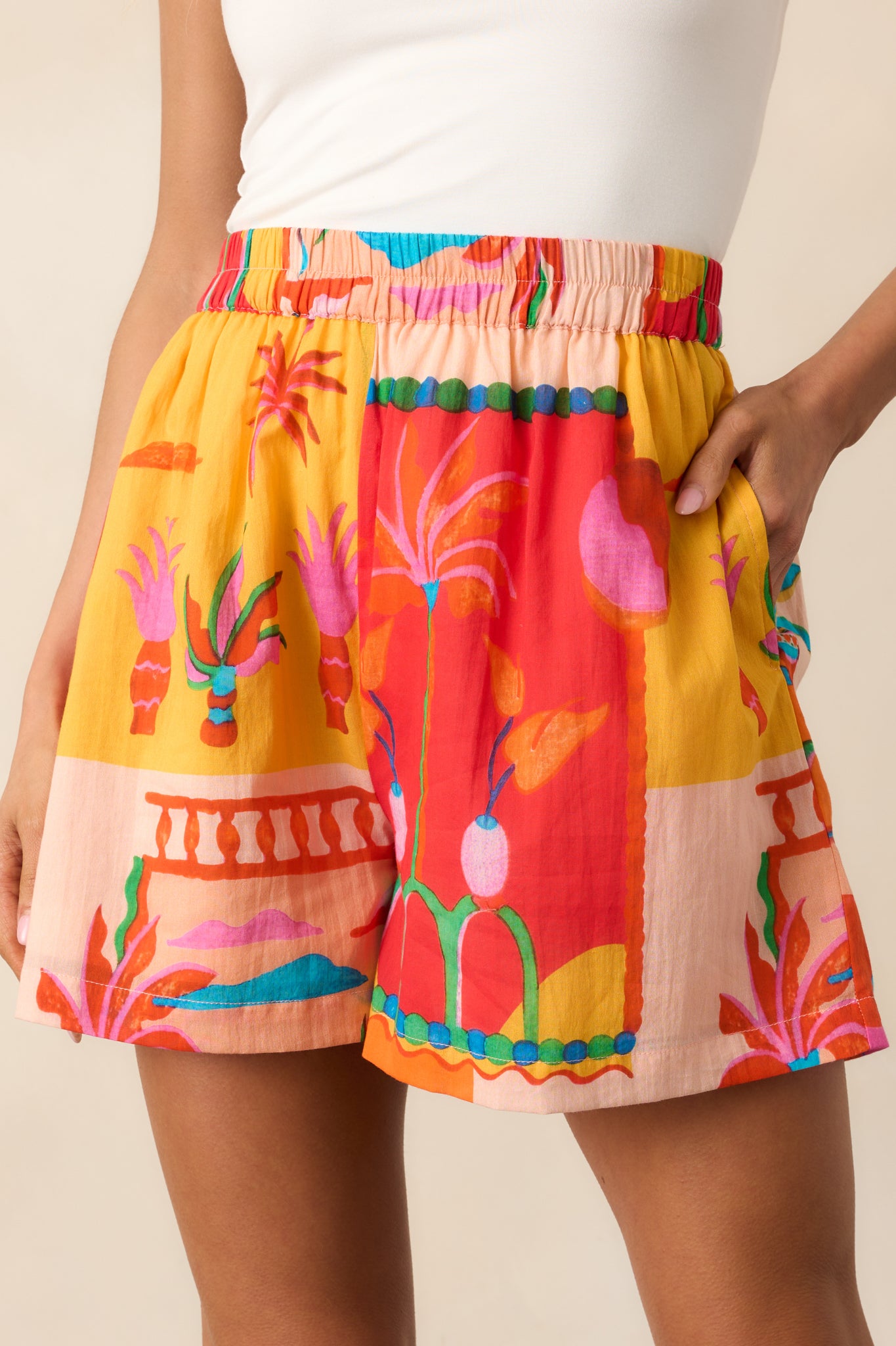 Cropped image showing the vibrant tropical pattern on the orange shorts and the relaxed, breezy fit.