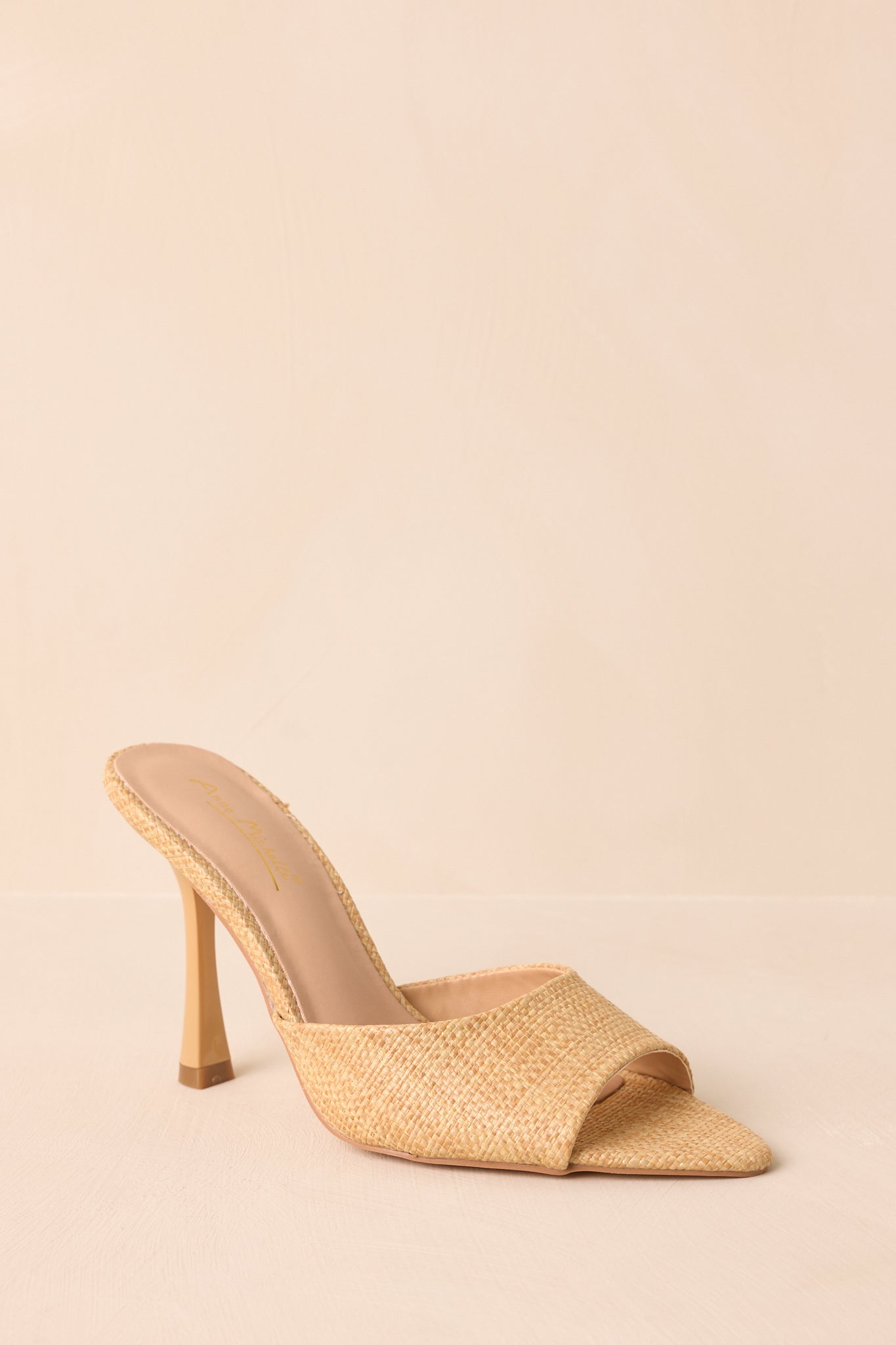A cropped view of the natural-colored open-toe mule heel, showing the faux raffia texture on the upper and stiletto heel.