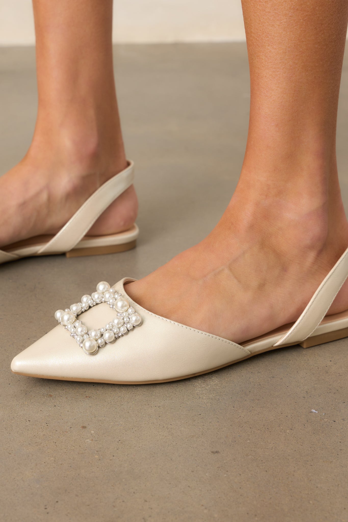 Cropped side view of the flats, highlighting the pointed toe, slip-on design, and the tan sole with a large rhinestone buckle on the toe.