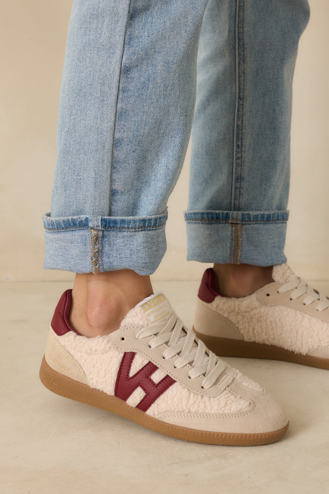 Cropped view highlighting the padded collar, lace-up front, and curved silhouette of the beige and burgundy sneakers.