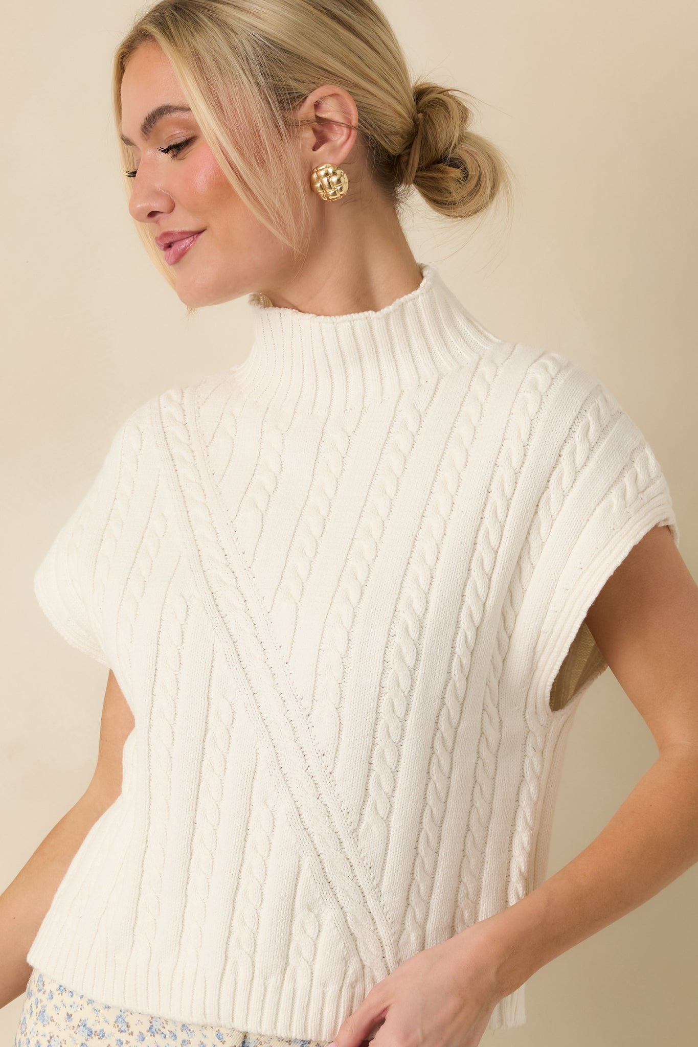 Cropped front view of an ivory cable knit sweater emphasizing the mock neckline and detailed cable pattern.