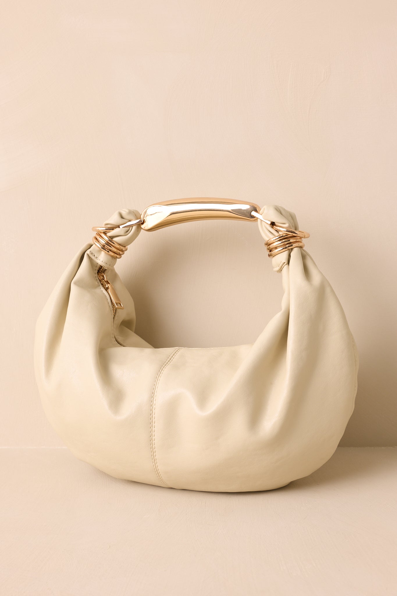 A cropped view focusing on the gold top handle and zipper closure of the ruched handbag.