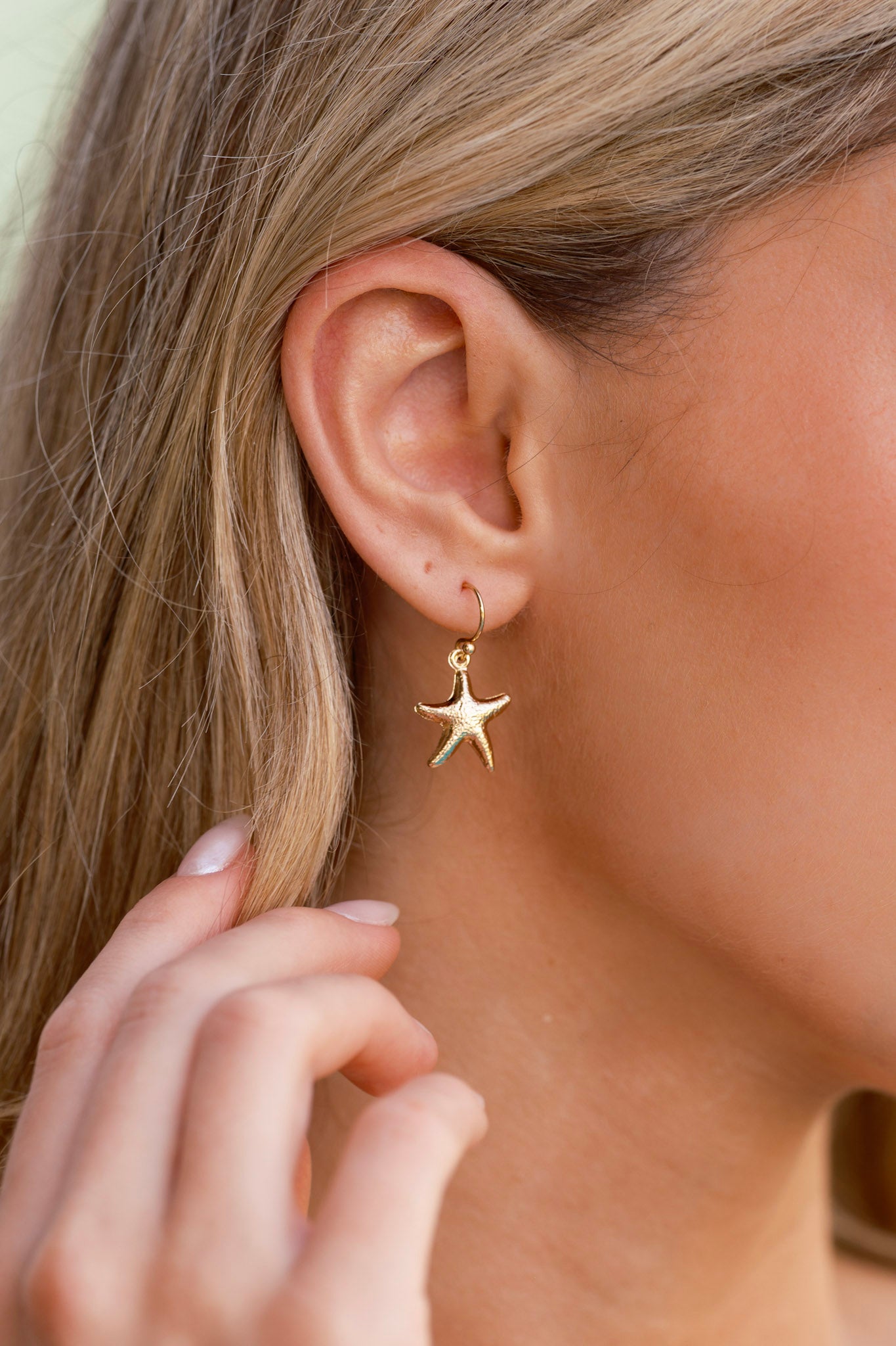 Cropped view of gold dangle earrings worn, highlighting the small starfish pendants and their subtle textured finish