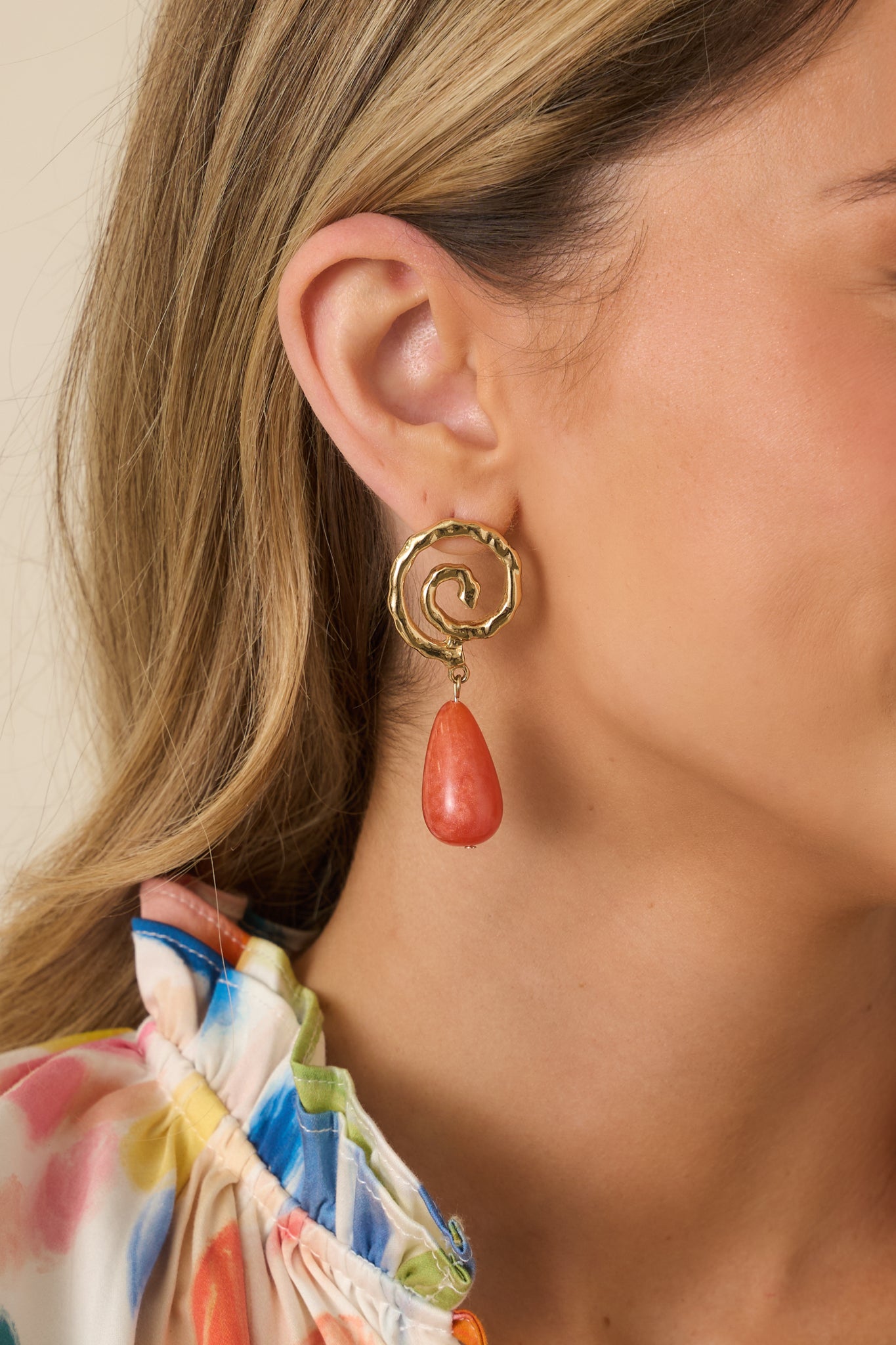 Cropped view of earrings showing hammered gold swirl stud and terracotta pearlescent drop charm.
