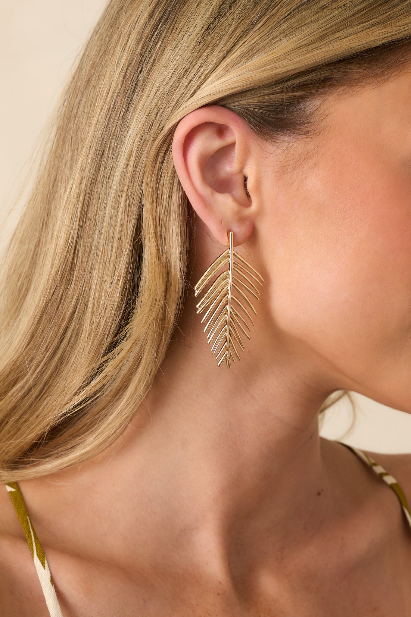 Cropped view of the gold drop earrings showing the curved palm leaf shape with textured ridges and smooth finish.