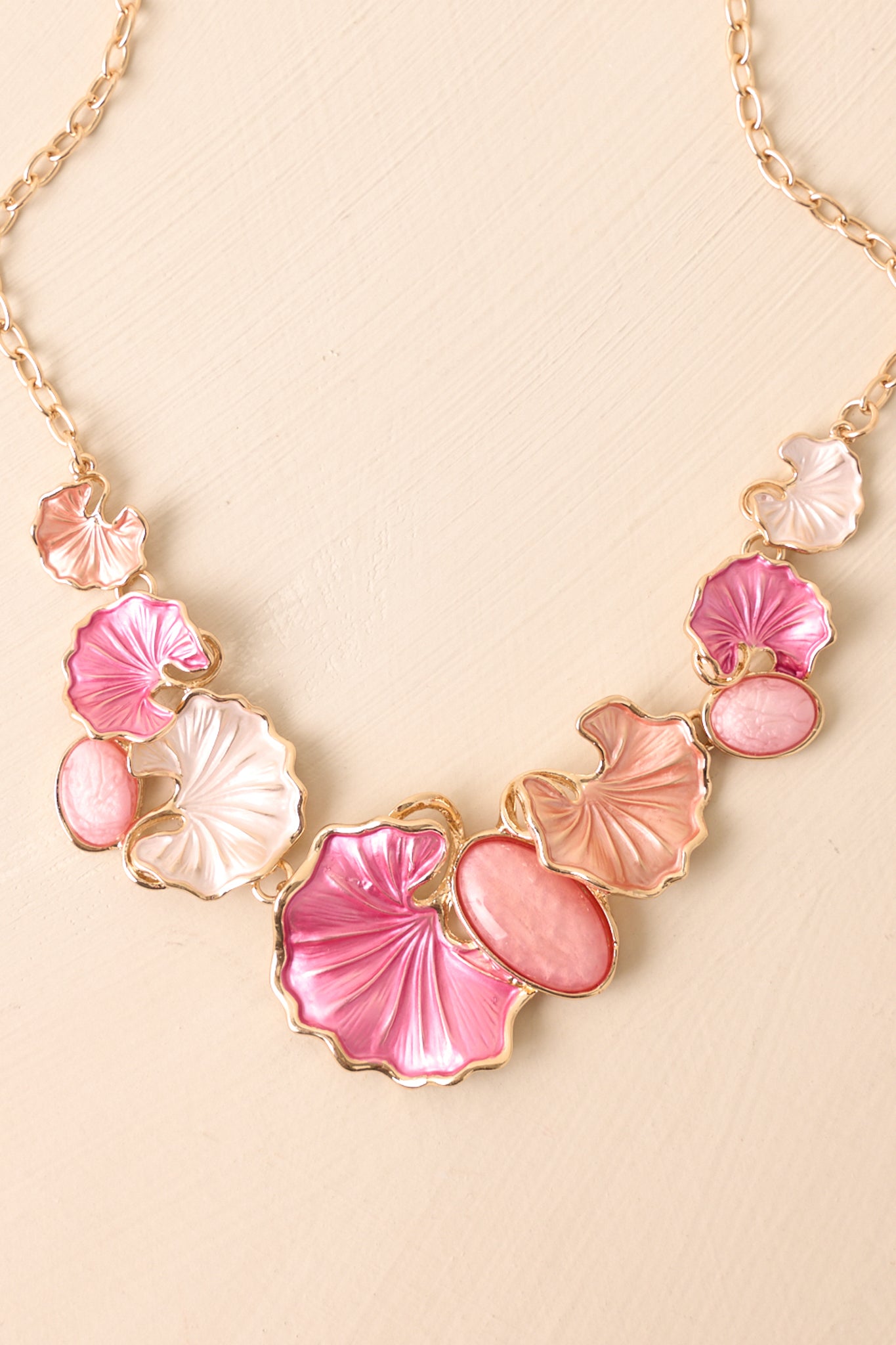 Close view of the pearlescent flower petal charms and gold chain accents on the pink bib necklace.