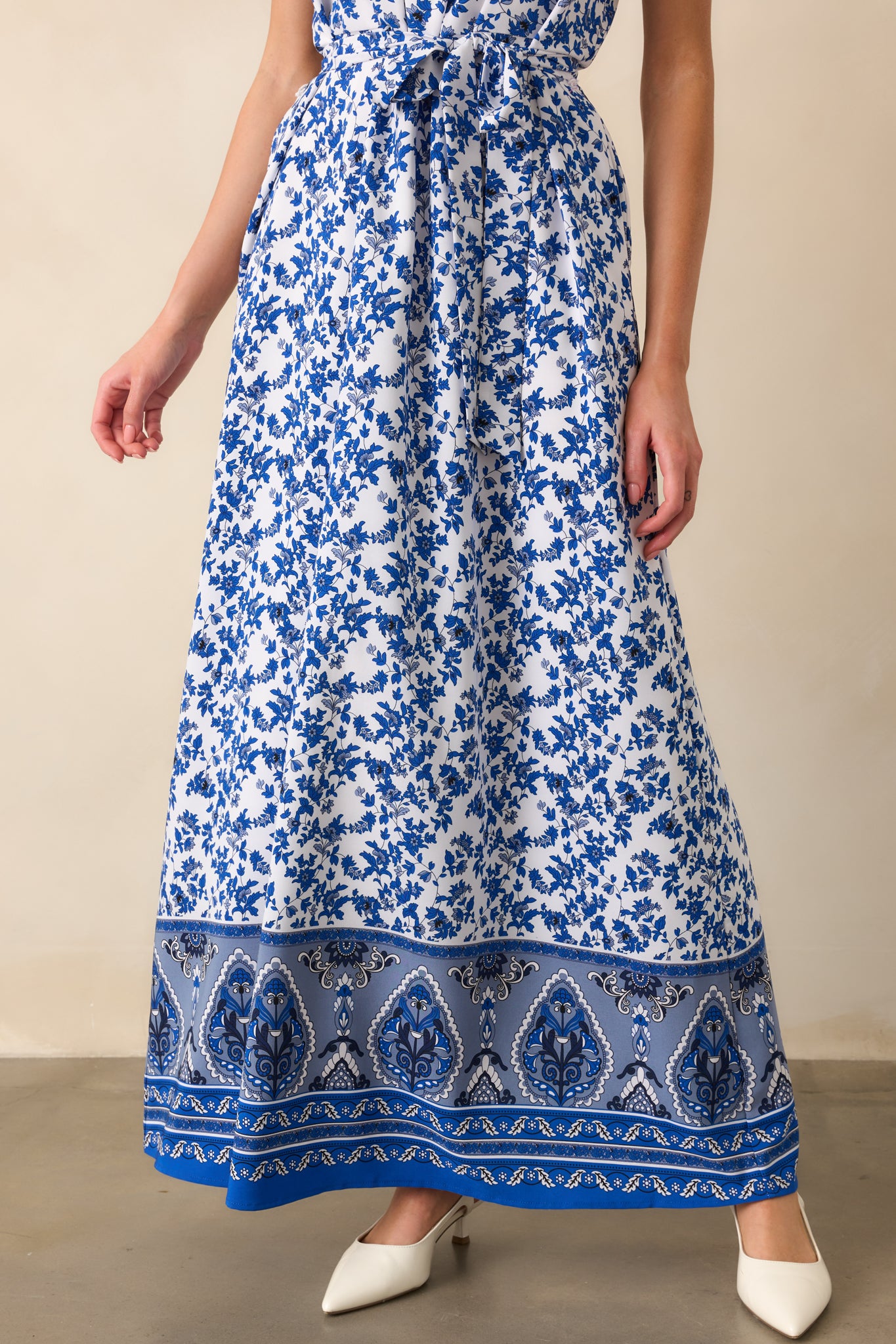 Cropped view of the dress from the waist down, highlighting the matching tie belt, functional side pockets, and the flow of the blue floral skirt.