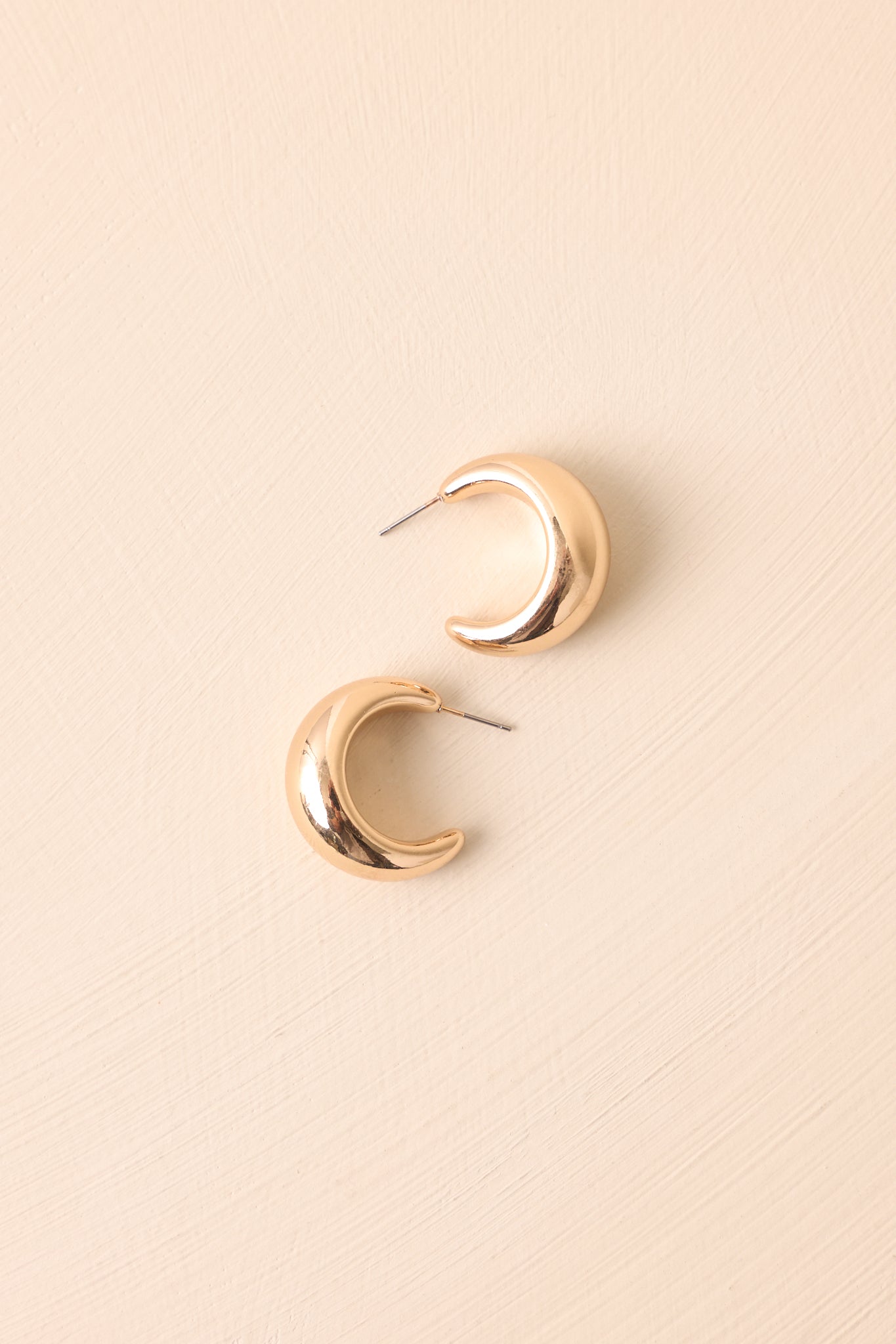 A cropped view of the shiny gold dome hoop earrings with an open silhouette.