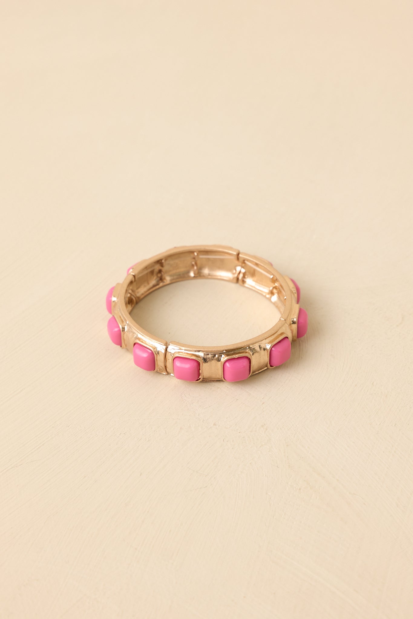 Cropped view of pink and gold-tone stretch bracelet featuring structured metal sections with pink square cabochon details.