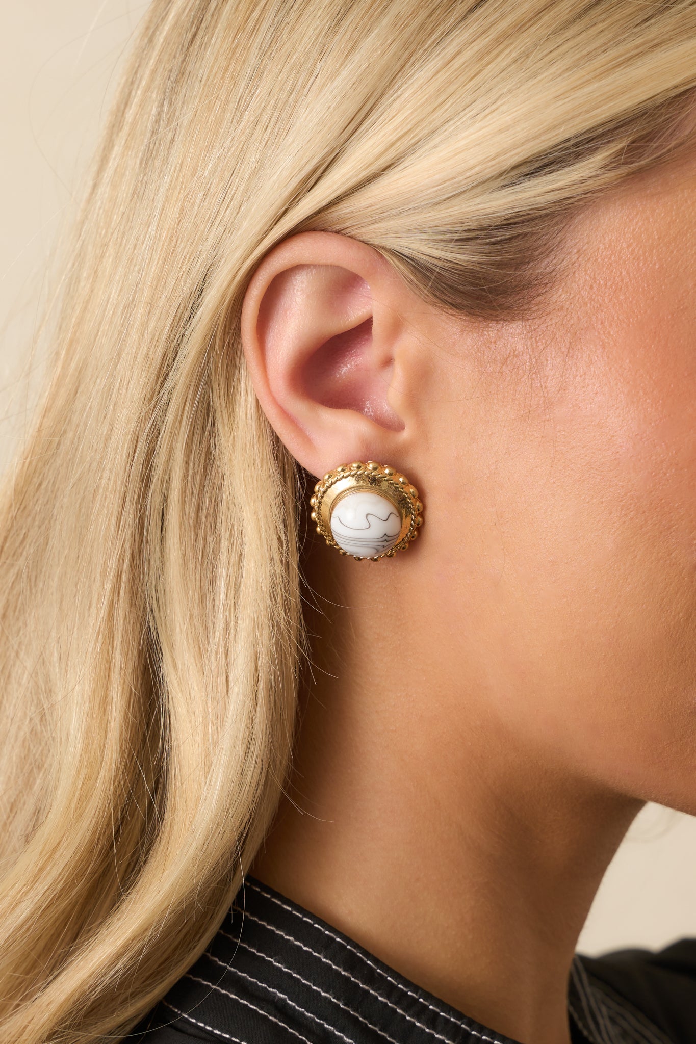 A cropped view showing circular gold stud earrings with a large howlite center and gold beaded border.