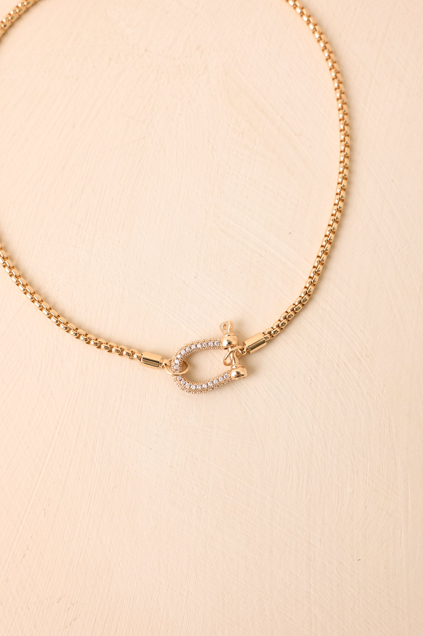 Close-up detail of the necklace showcasing the crystal pavé shackle clasp, reflective gold-tone finish, and intricate decorative accents.