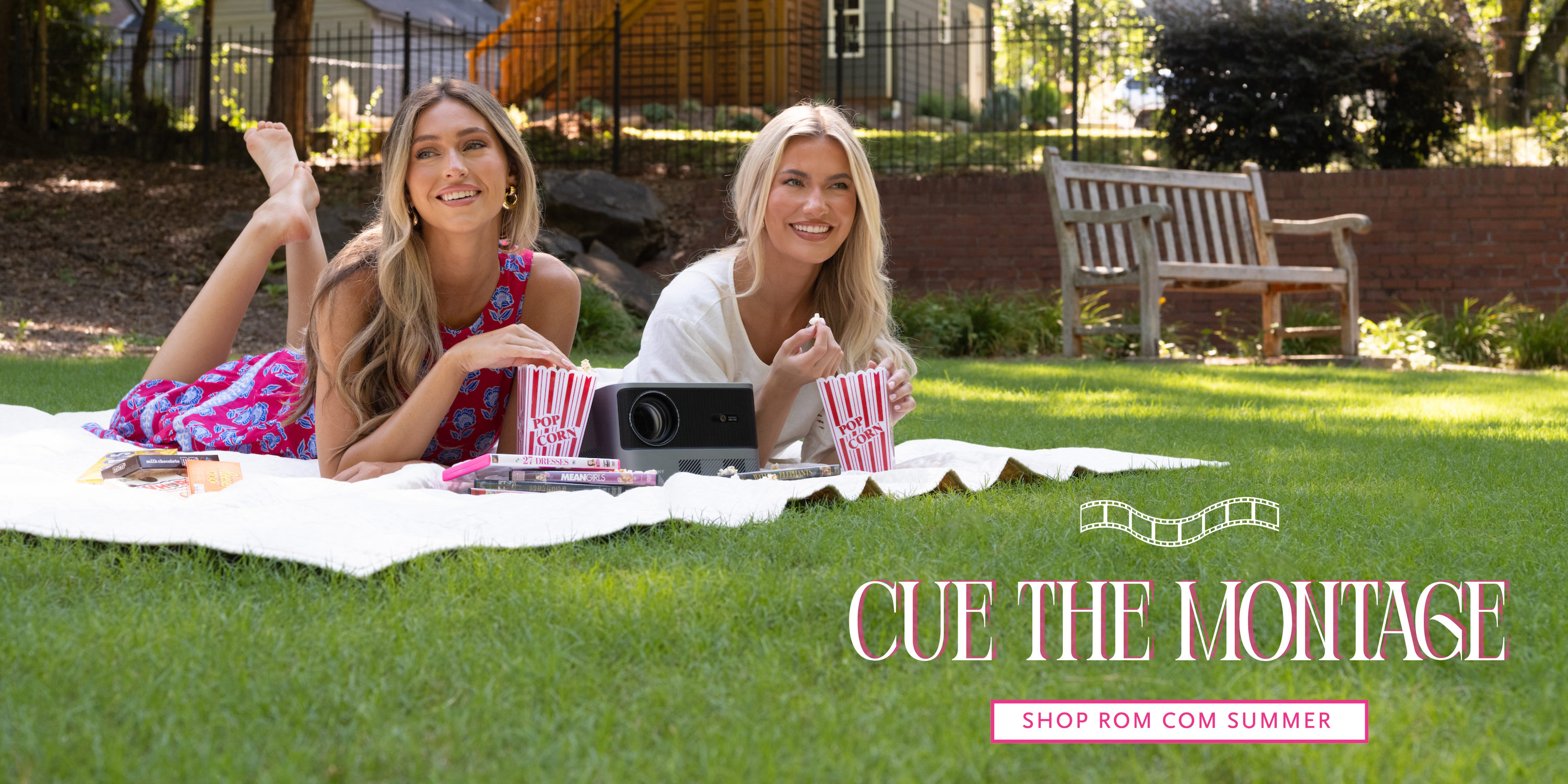 Two models in vibrant summer outfits enjoy an outdoor movie night on a picnic blanket with popcorn, candy, and a projector. Text reads: "Cue the Montage. Shop ROM Com Summer."
